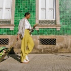 Vertical shot of black female tourist with suitcase walking in front a tiled green historical building checking her phone for directions on a sunny day carrying her luggage , License Type: media,