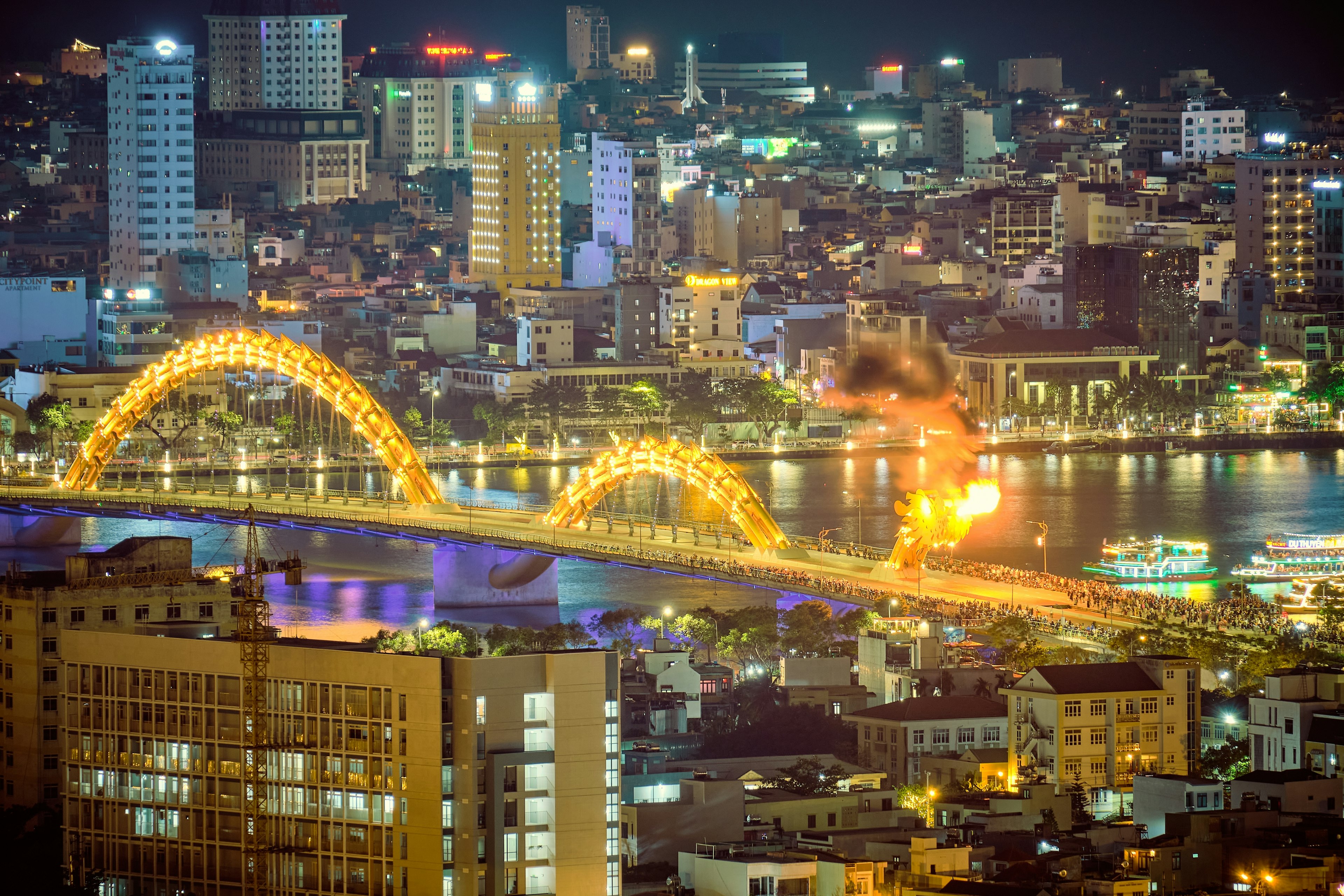 Crowds of people gather on a bridge shaped like a dragon while it breathes fire