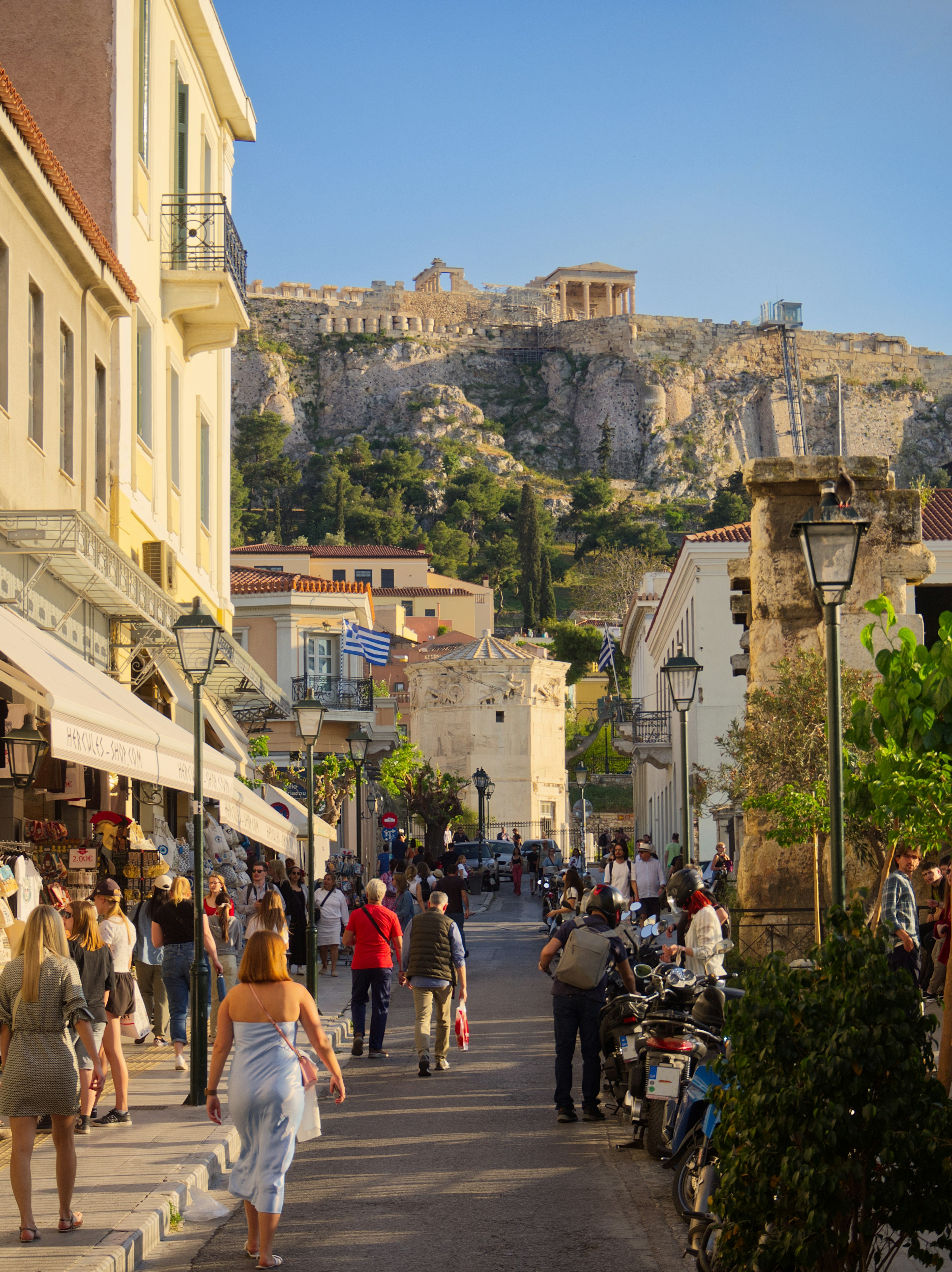 Plaka shopping street full of people with Acropolis in view under sunset colors