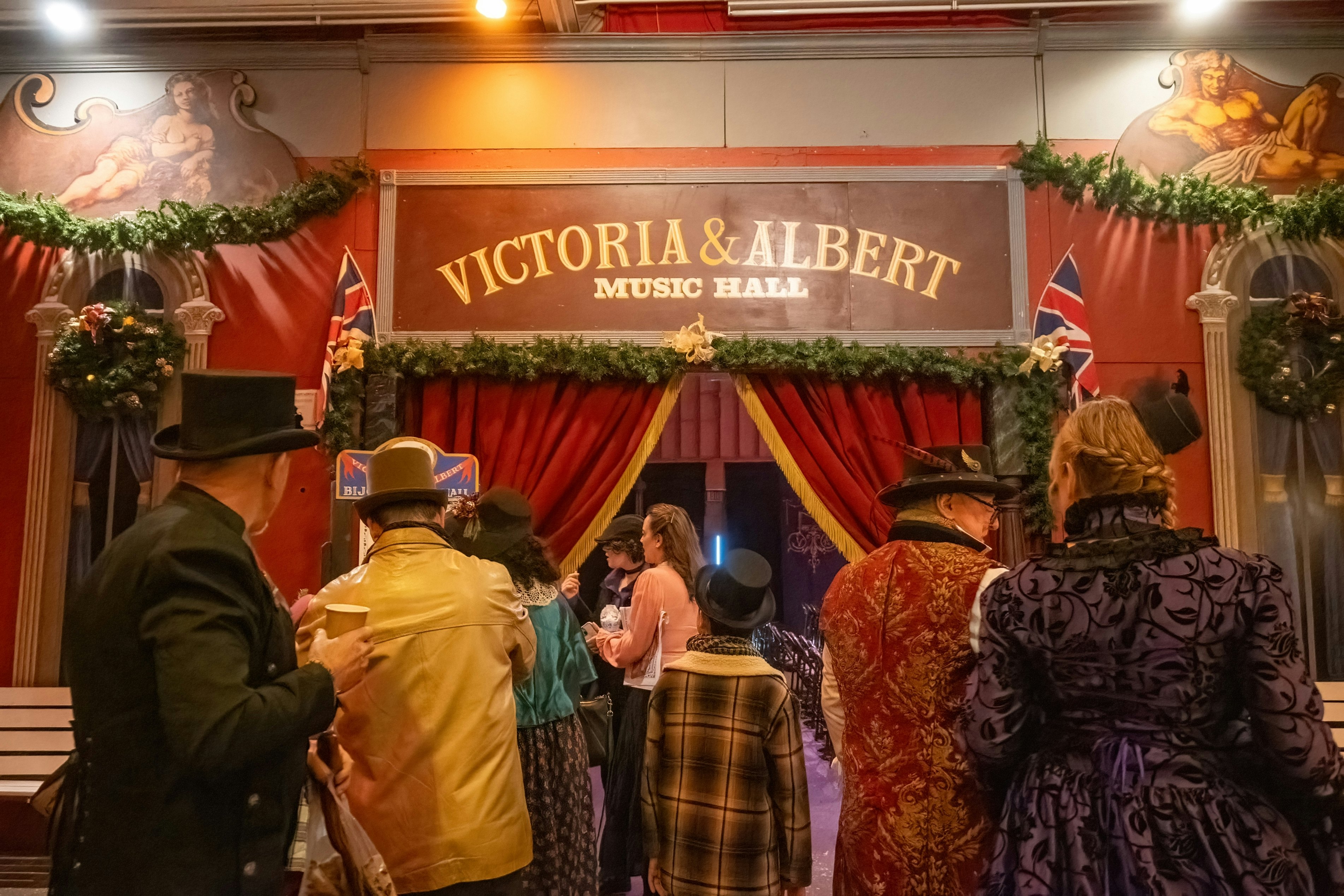 People in Victorian costume enter a curtained doorway with a sign that reads "Victoria and Albert Music Hall"