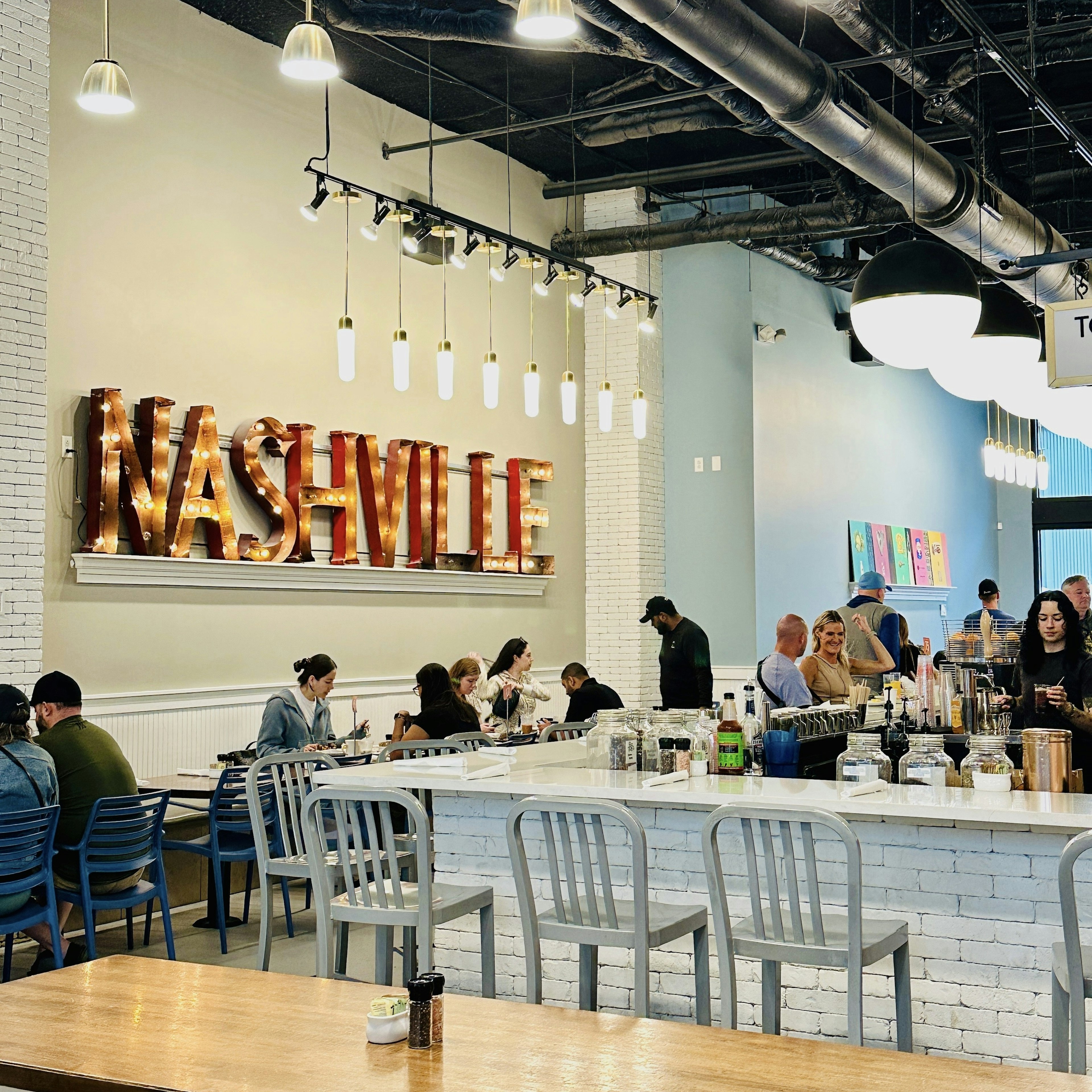 People sit in a sleek and modern restaurant enjoying food and drink with a bit sign spelling out “NASHVILLE” in light bulbs against one wall