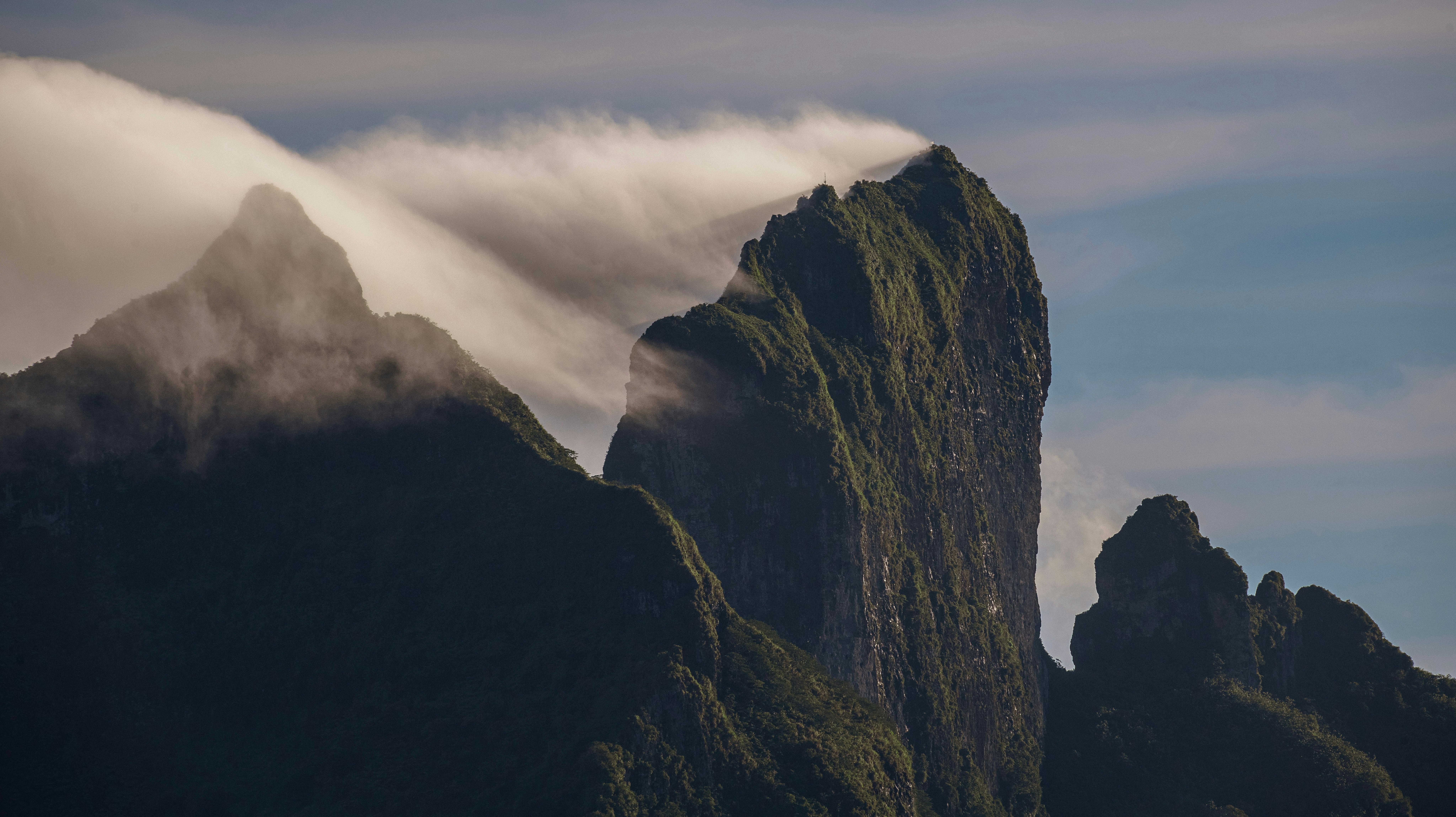 A close-up shot of misty clouds hugging rocky, spiky peaks of a mountain on a tropical island