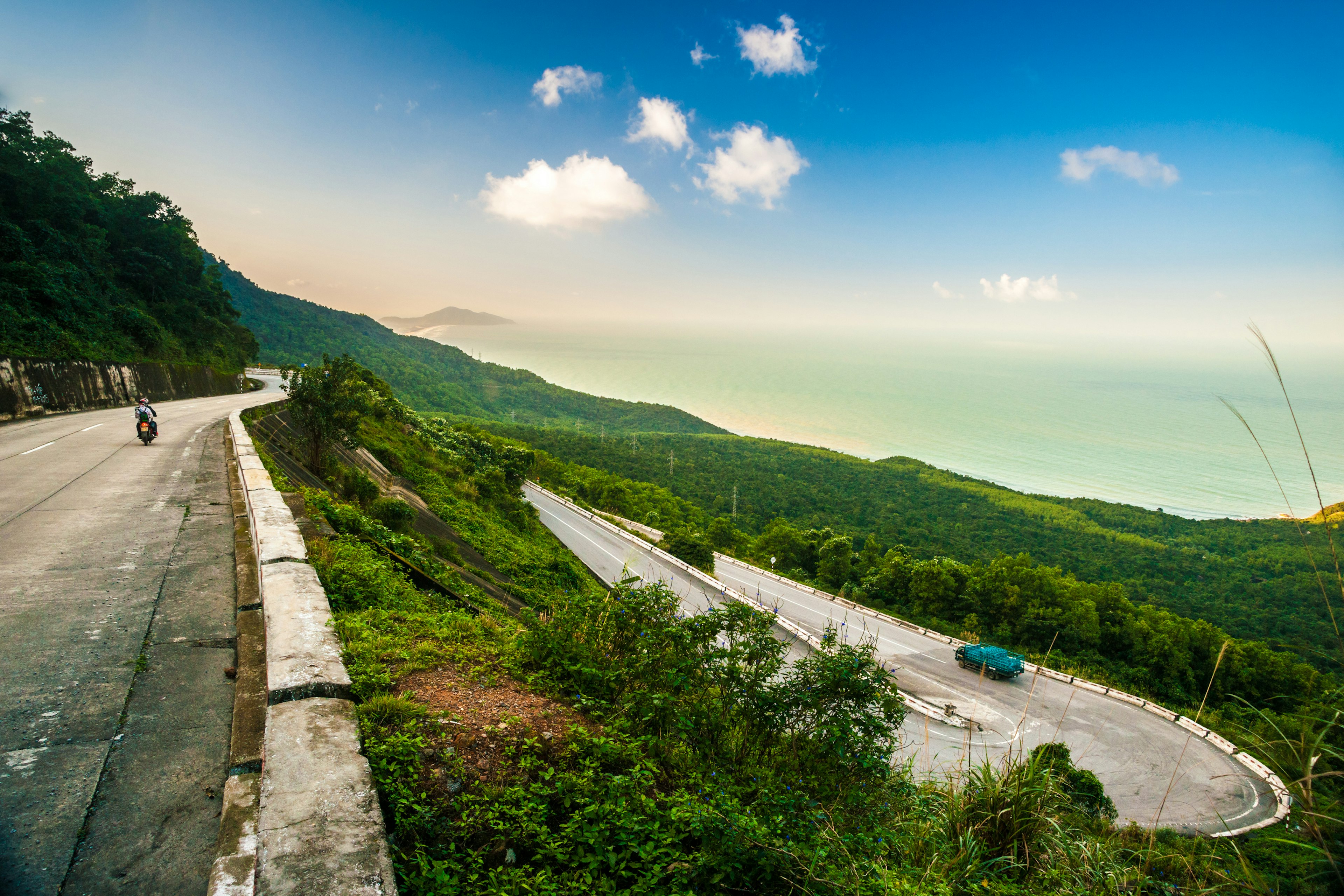 A motorcycle travels along a coastal mountain road with switchbacks