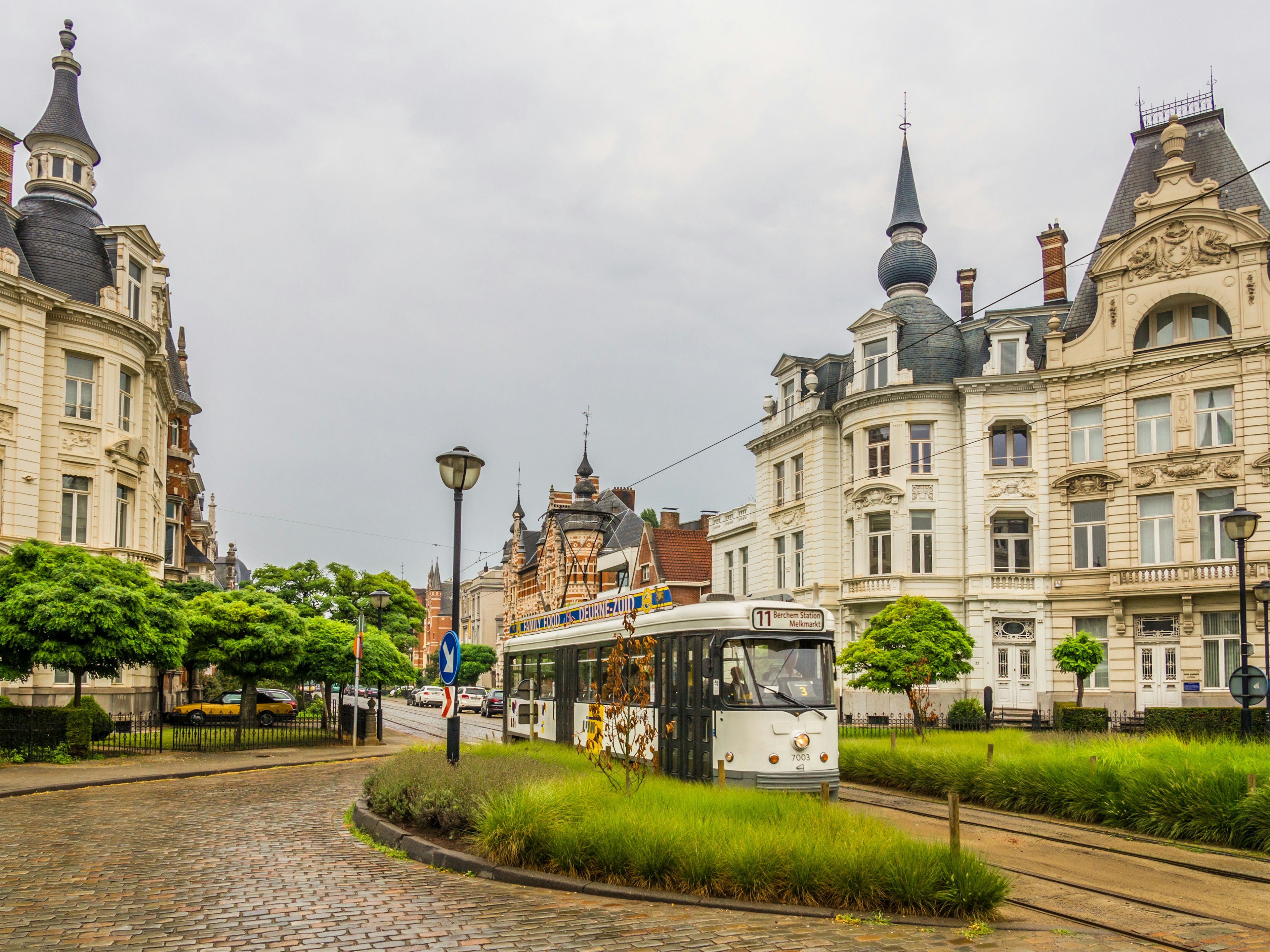 A tram runs down a street lined with grand mansions