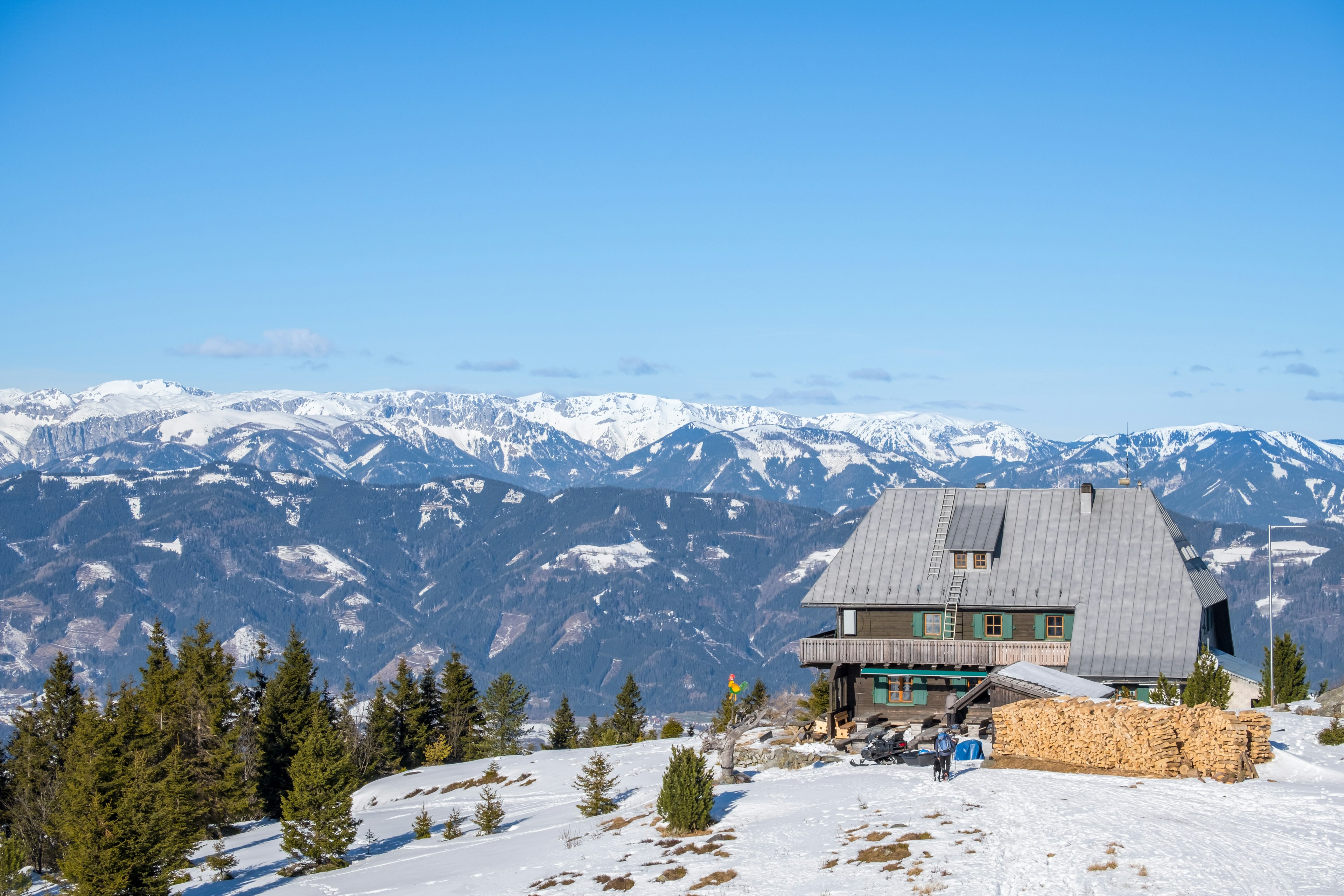 A hut from the snowy summit of mountain Rennfeld and the distant mountain tops of the Hochschwab mountain range in winter.