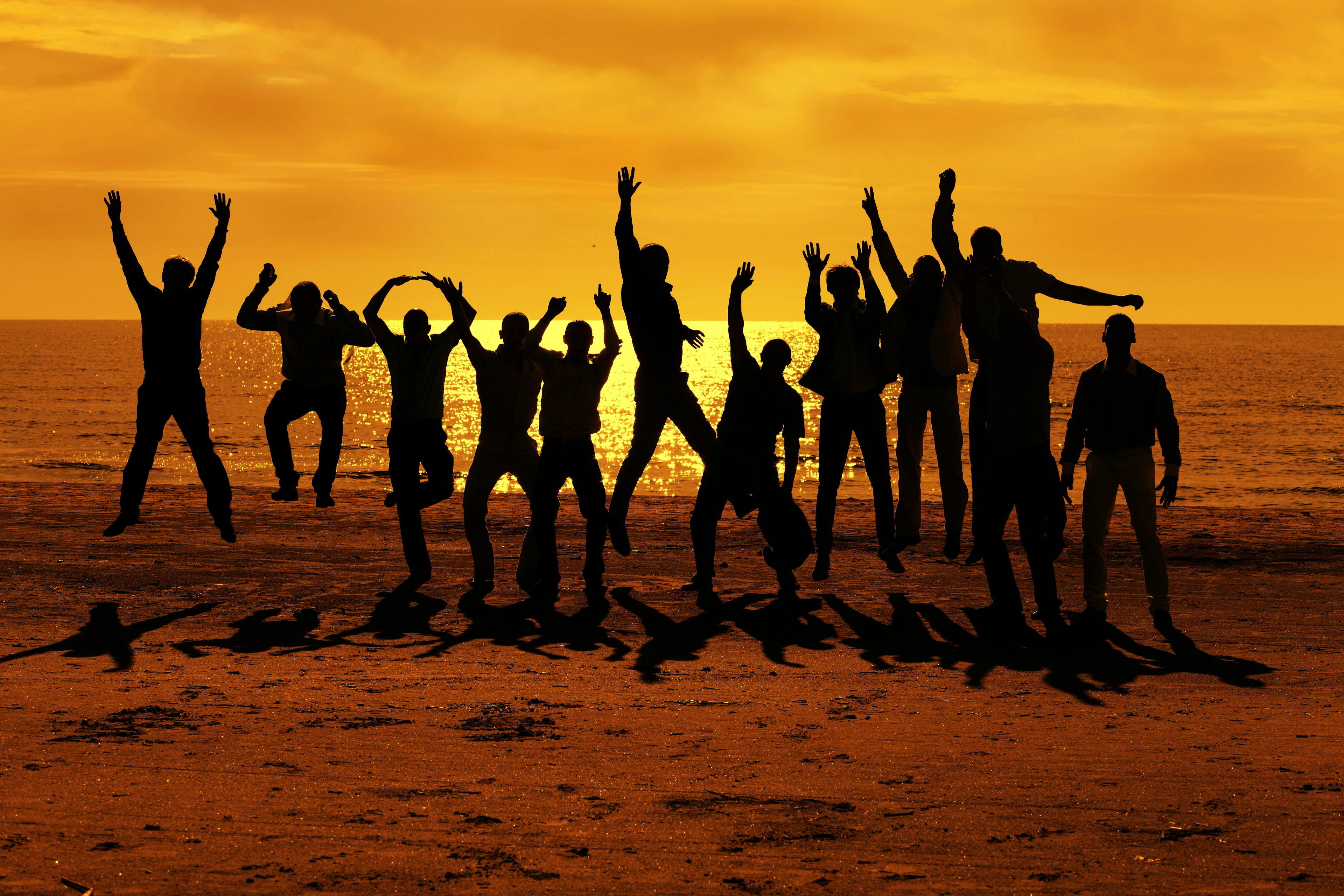 Silhouette of male friends jumping together during sunset on the beach. 