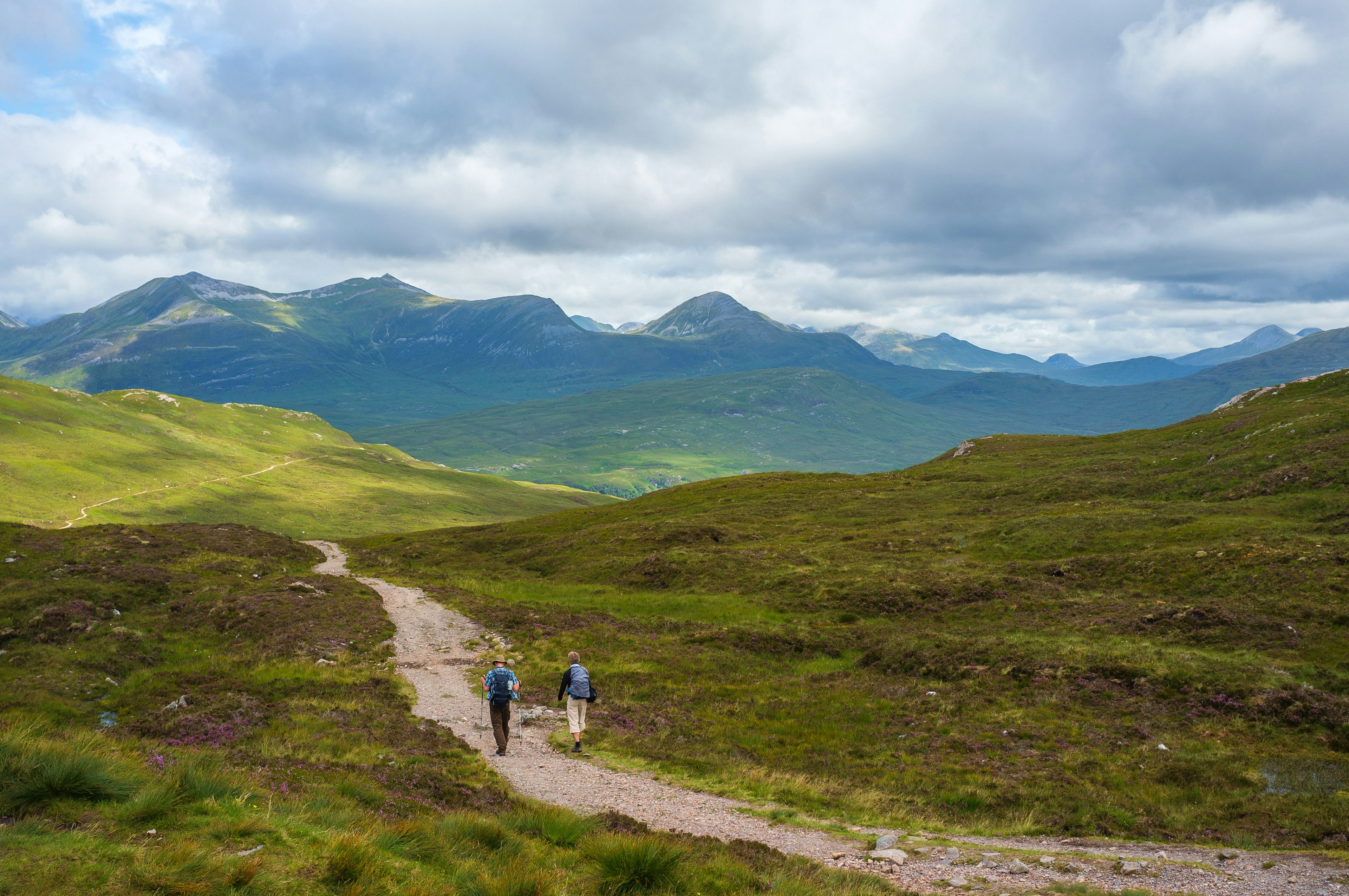 Two hikers follow a path leading through mountains