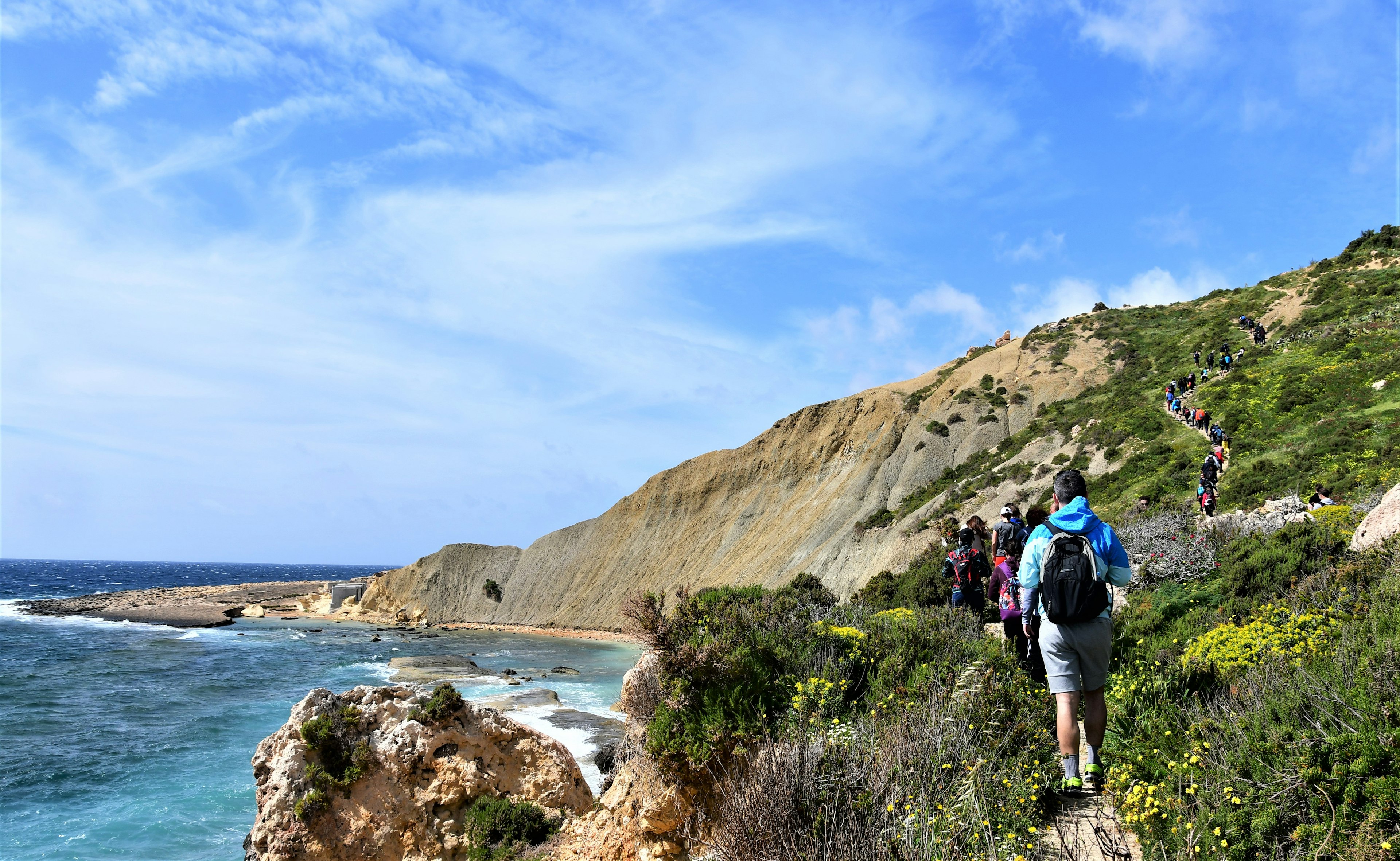 A line of hikers ascend a grass-covered hill on the coast of Gozo island.