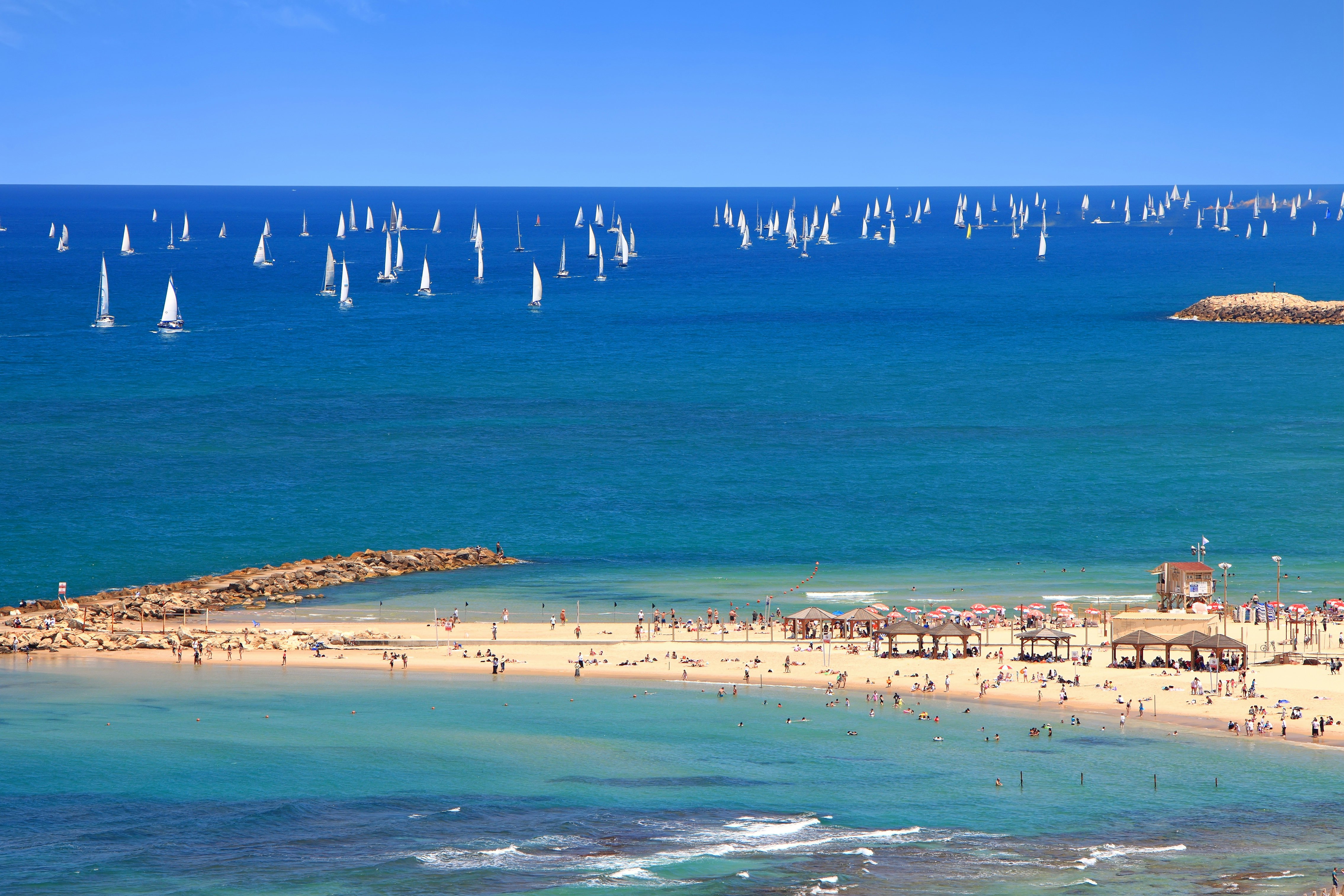 People crowd a Tel-Aviv beach with many yachts in the Mediterranean sea beyond.