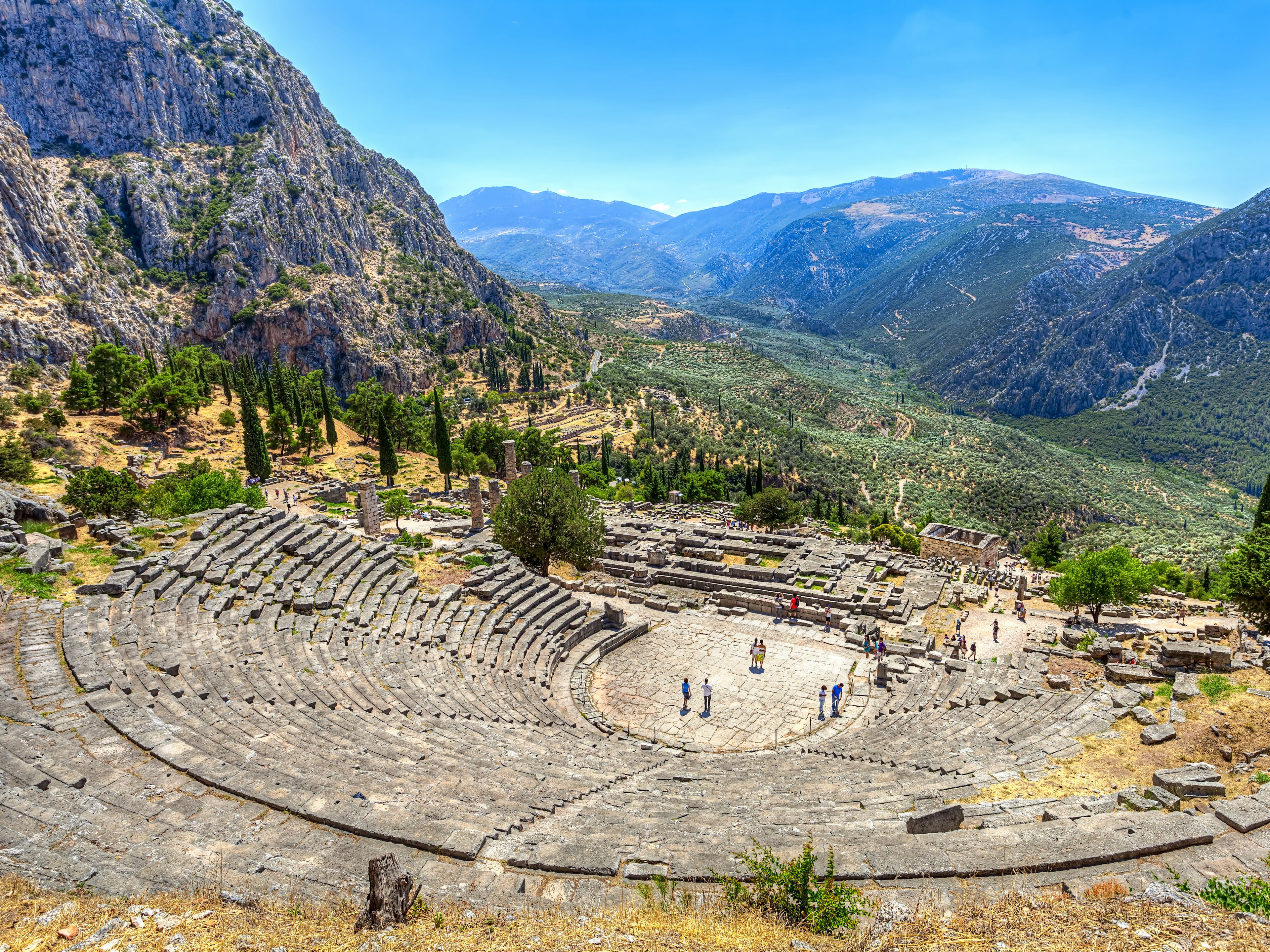 A massive ancient Greek amphitheater with mountains in the background.