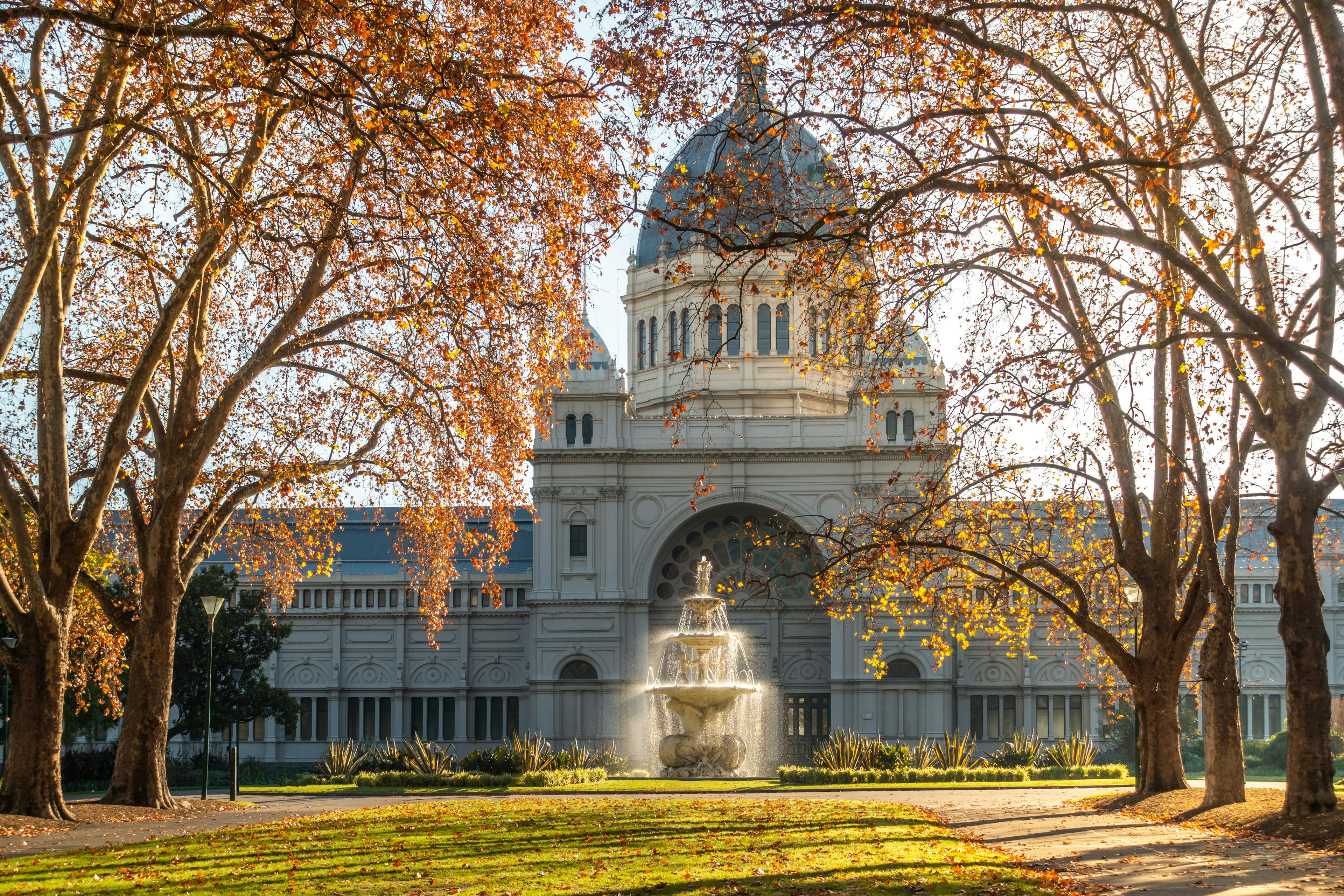 Historic Royal Exhibition Building and autumn trees bathed in morning sunlight in Carlton Gardens.