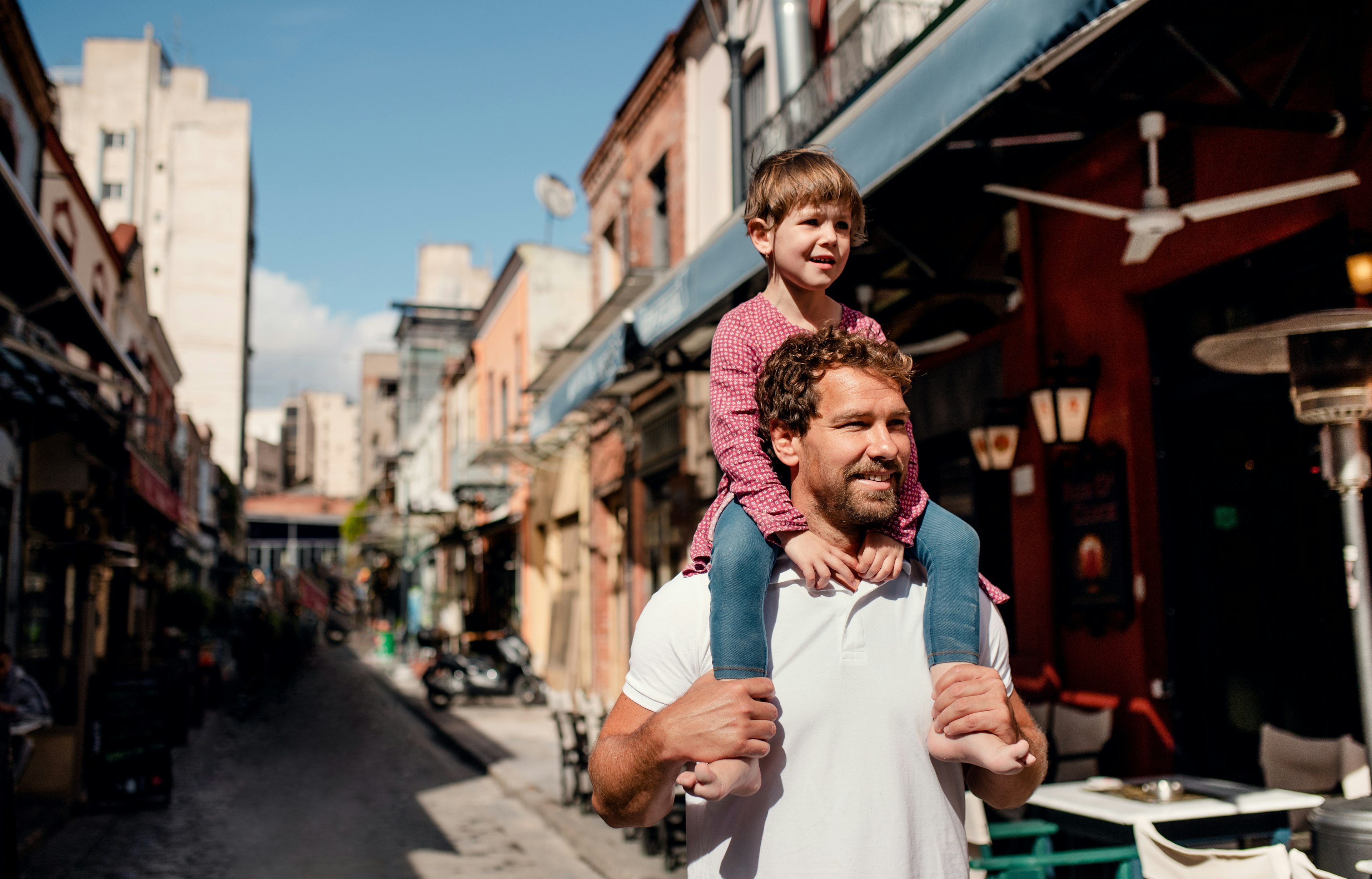 Father carrying his small daughter on his shoulders in a Mediterranean town in Greece.