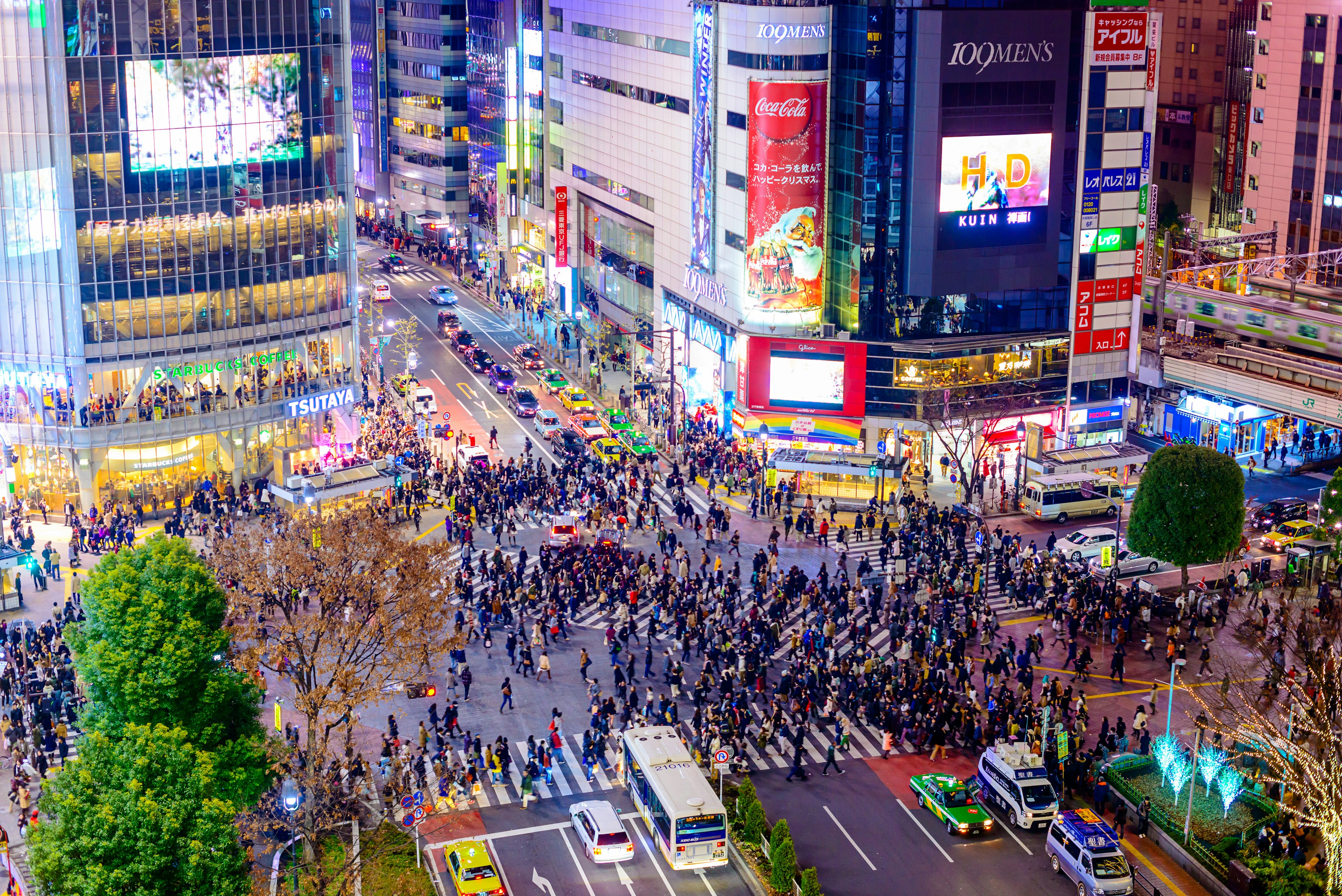 People crossing a massive interchange in a neon-lit city