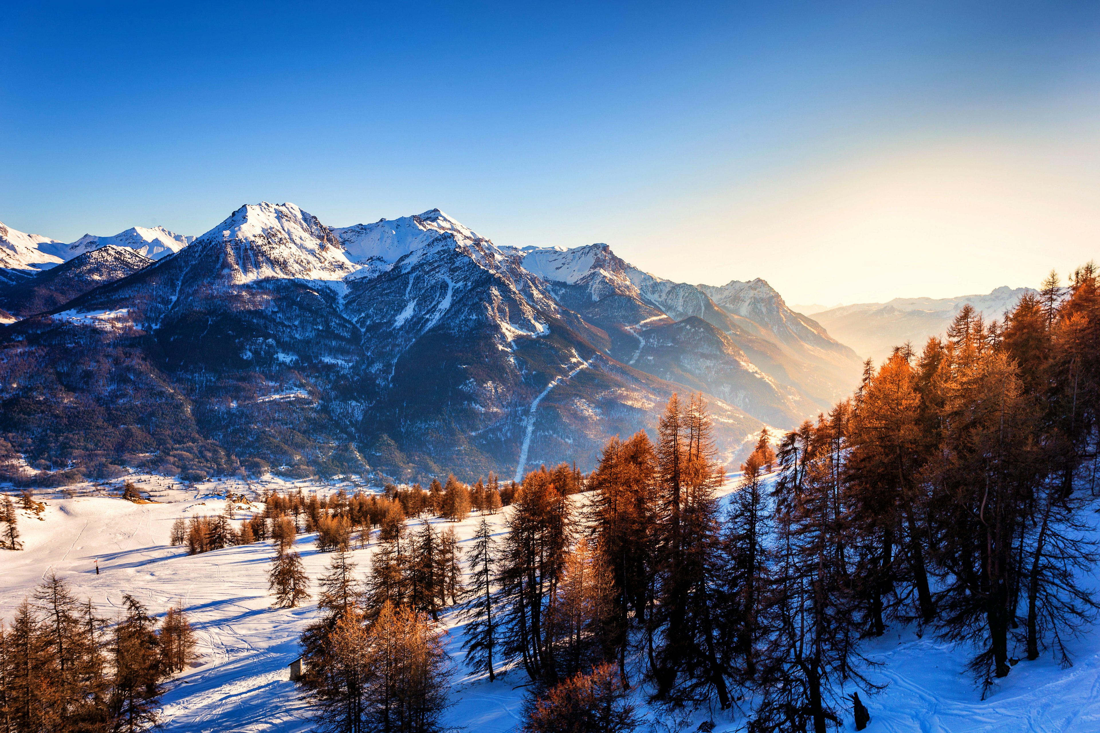 Frozen scene near a ski resort in the french alps just above Briancon in France, with blue sky before sunset in the golden hour over the mountain with fresh snow.