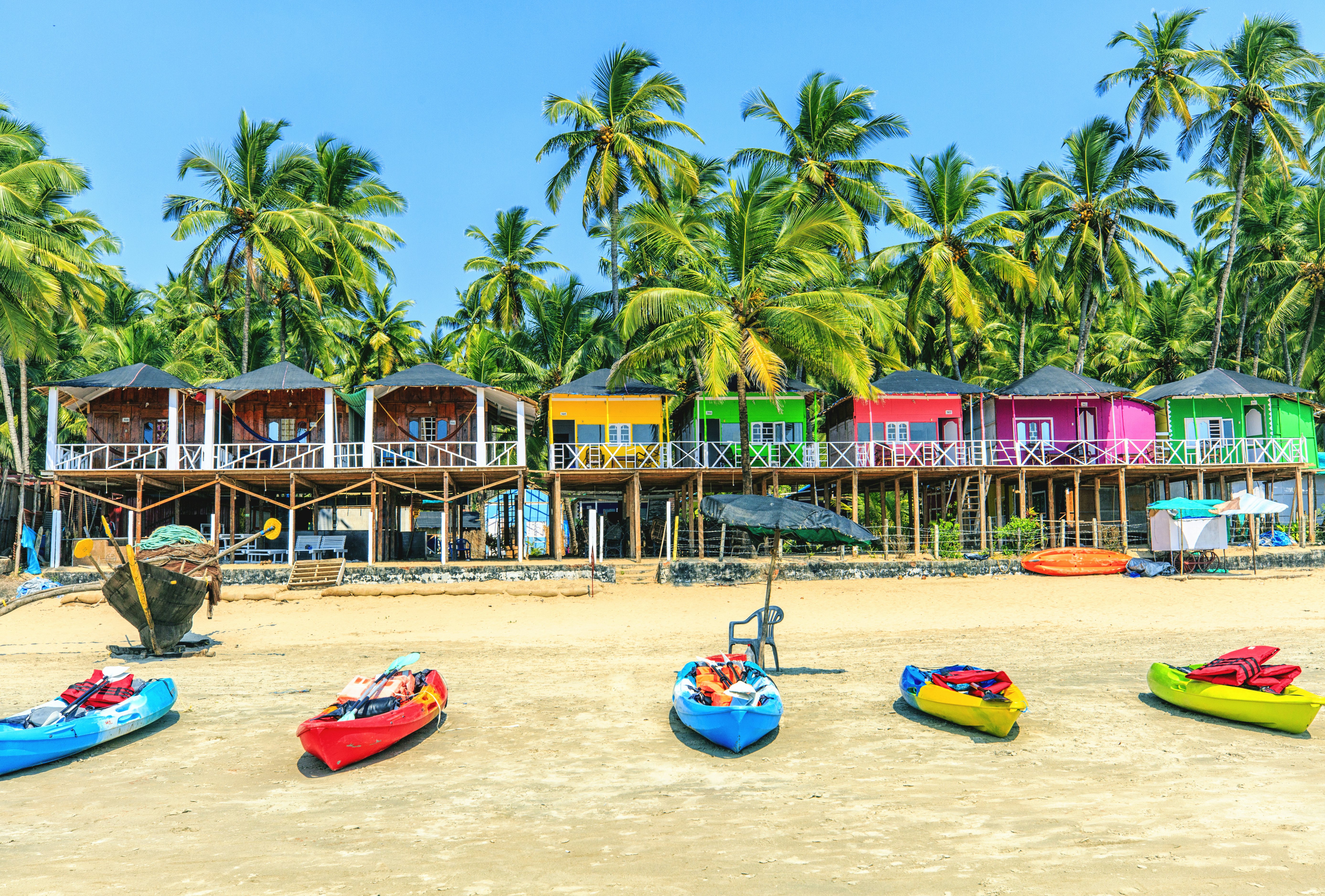 Colorful bungalows stand under palm trees on a beach and kayaks