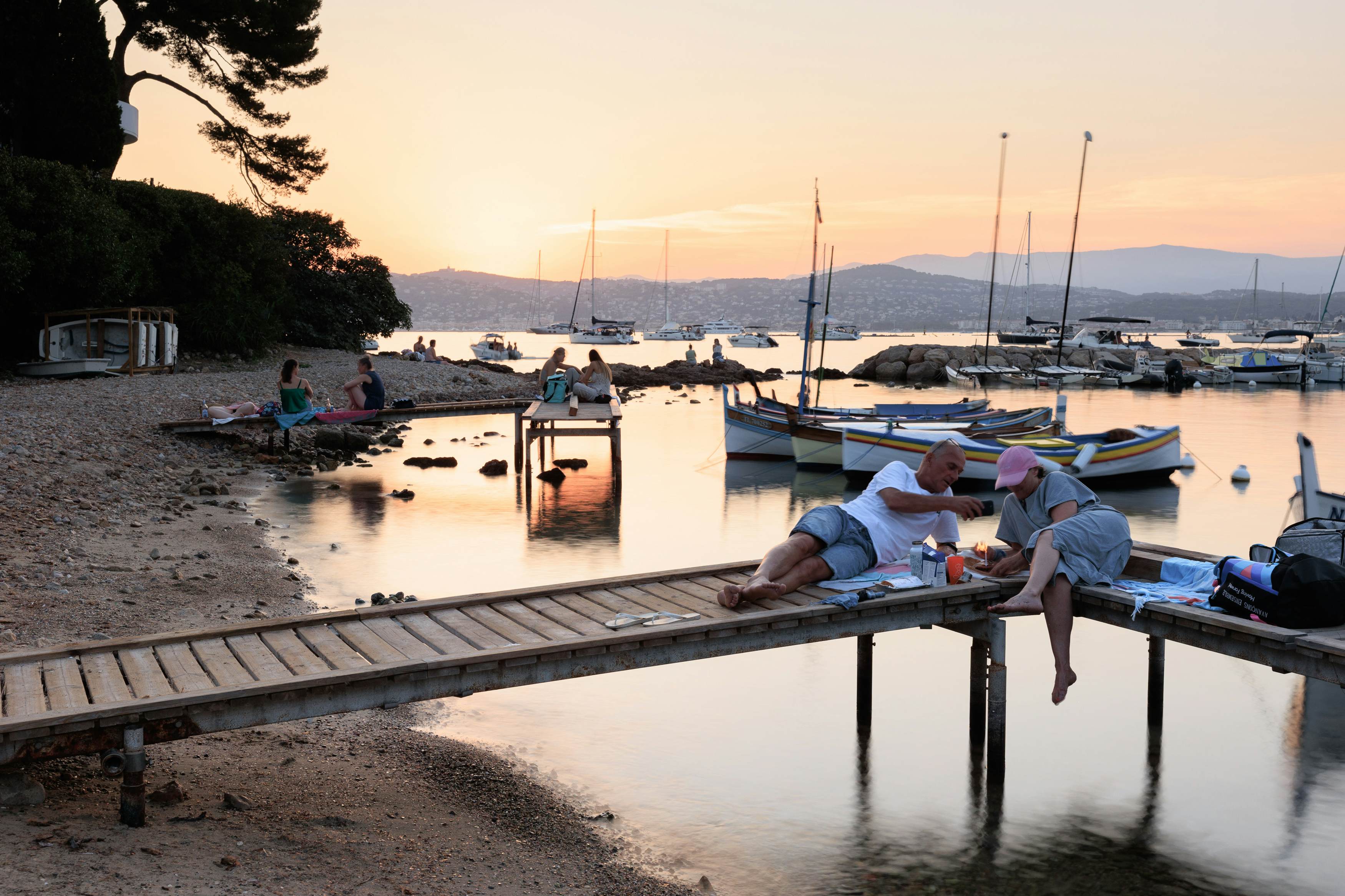 Couple picnicking on a pier at Cap d'Antibes, Antibes, France, July 27, 2024 at sunset with boats in the background