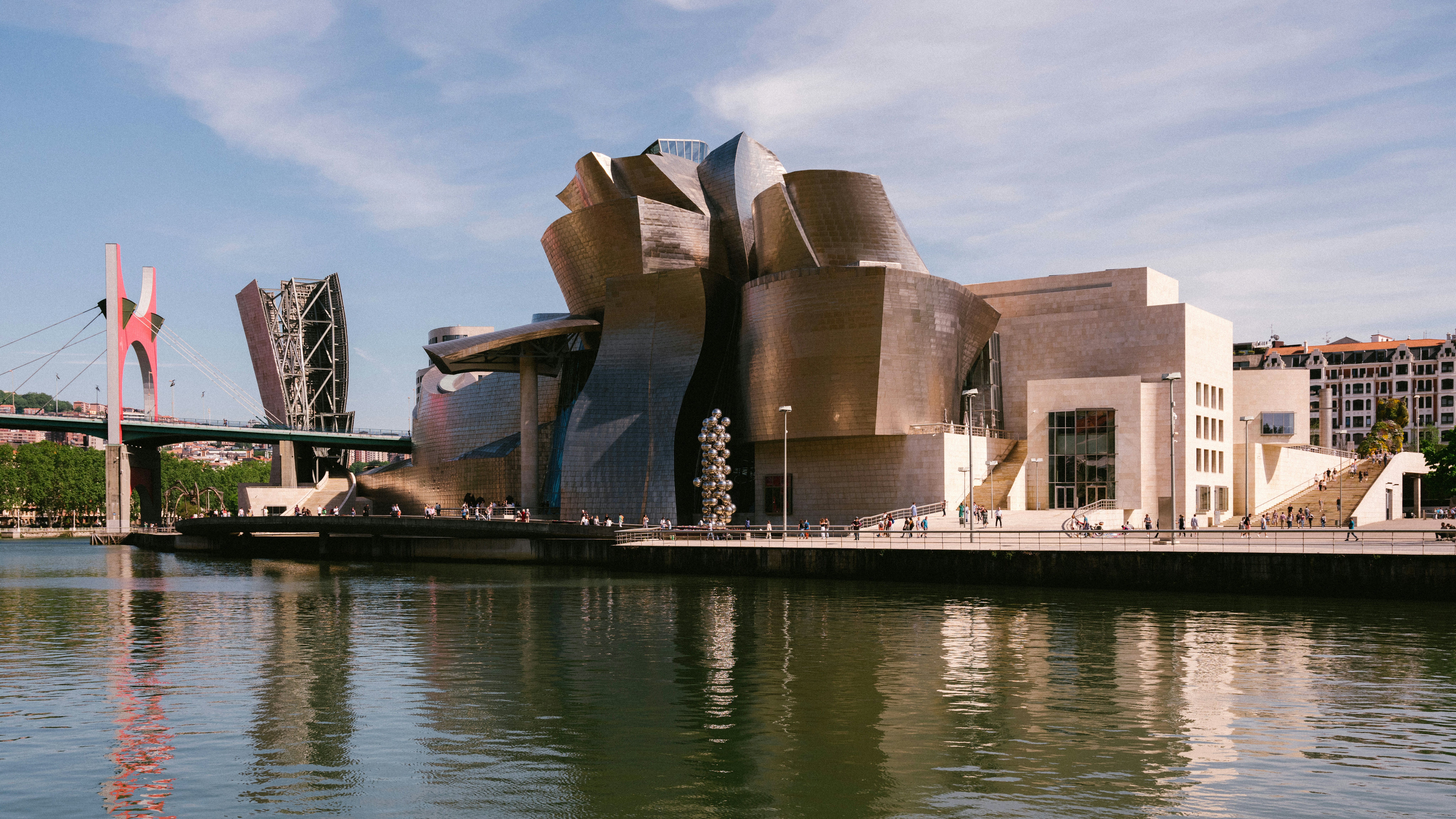 A futuristic building wrapped in metal panels is seen along a riverbank.