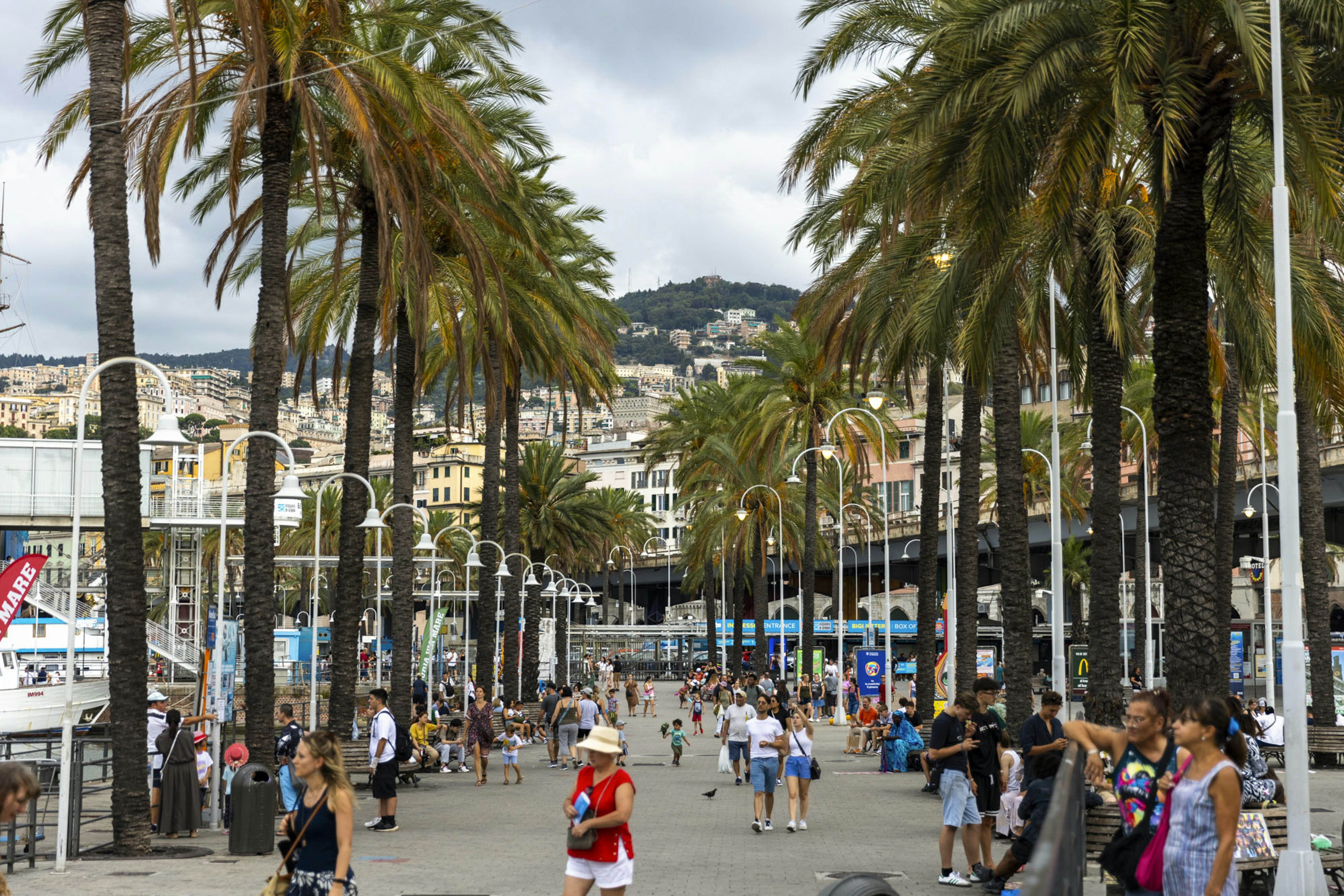 Crowds walk along Porto Antico of Genoa, with various details and exteriors.