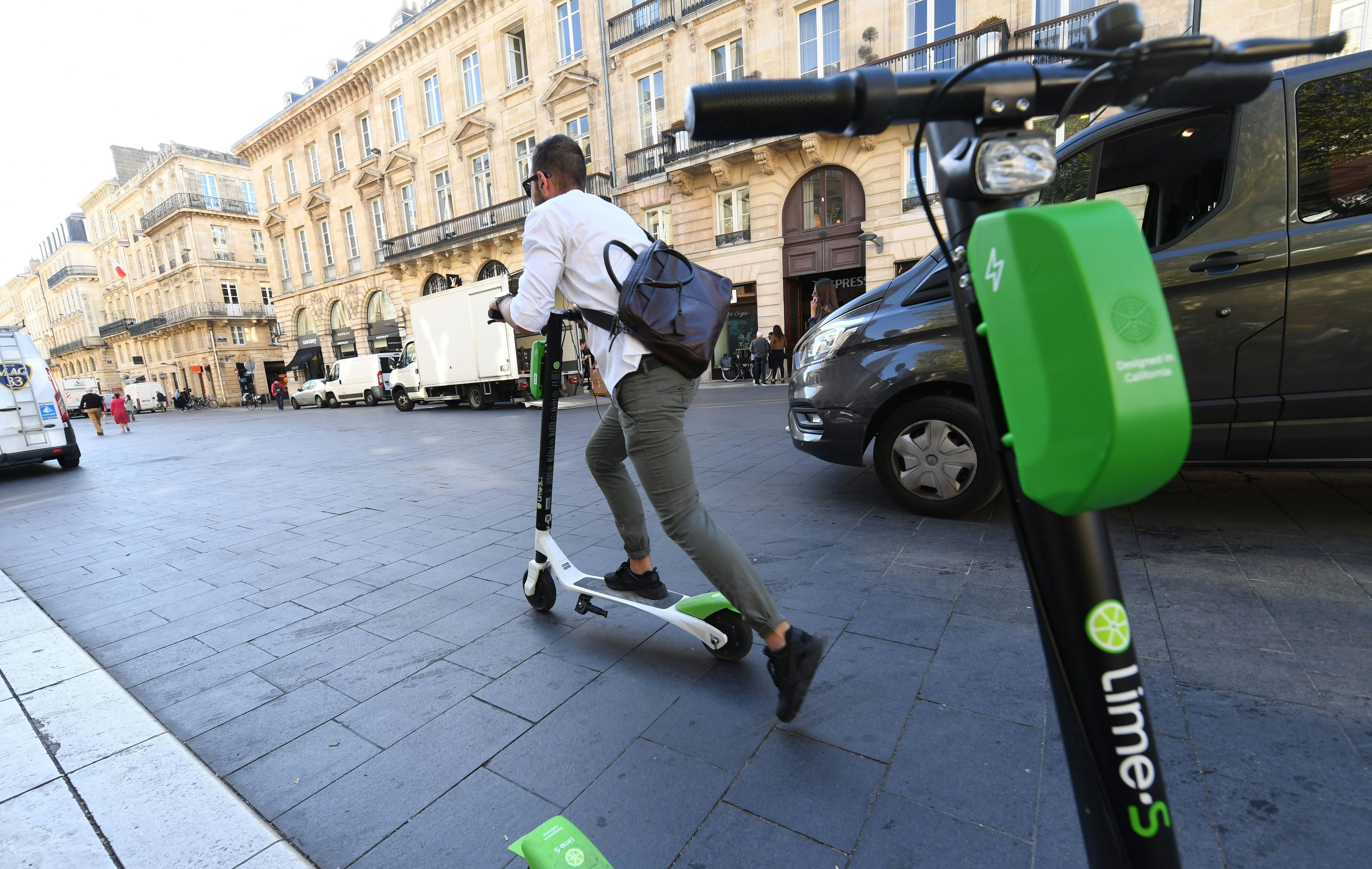 A man pushes on a scooter E without quay in a street in Bordeaux, in France. Another parked scooter is visible in the foreground.