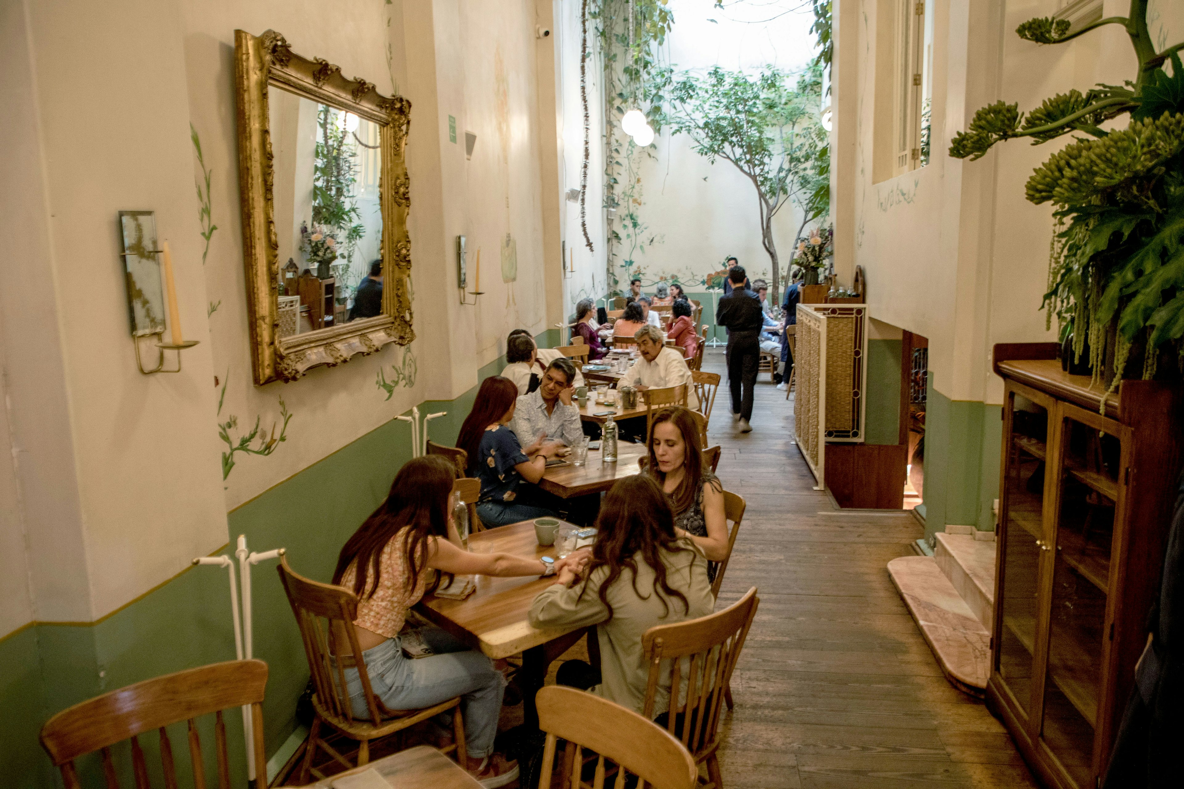 People sit at tables in a hallway dining area of a stylish restaurant in a historic home