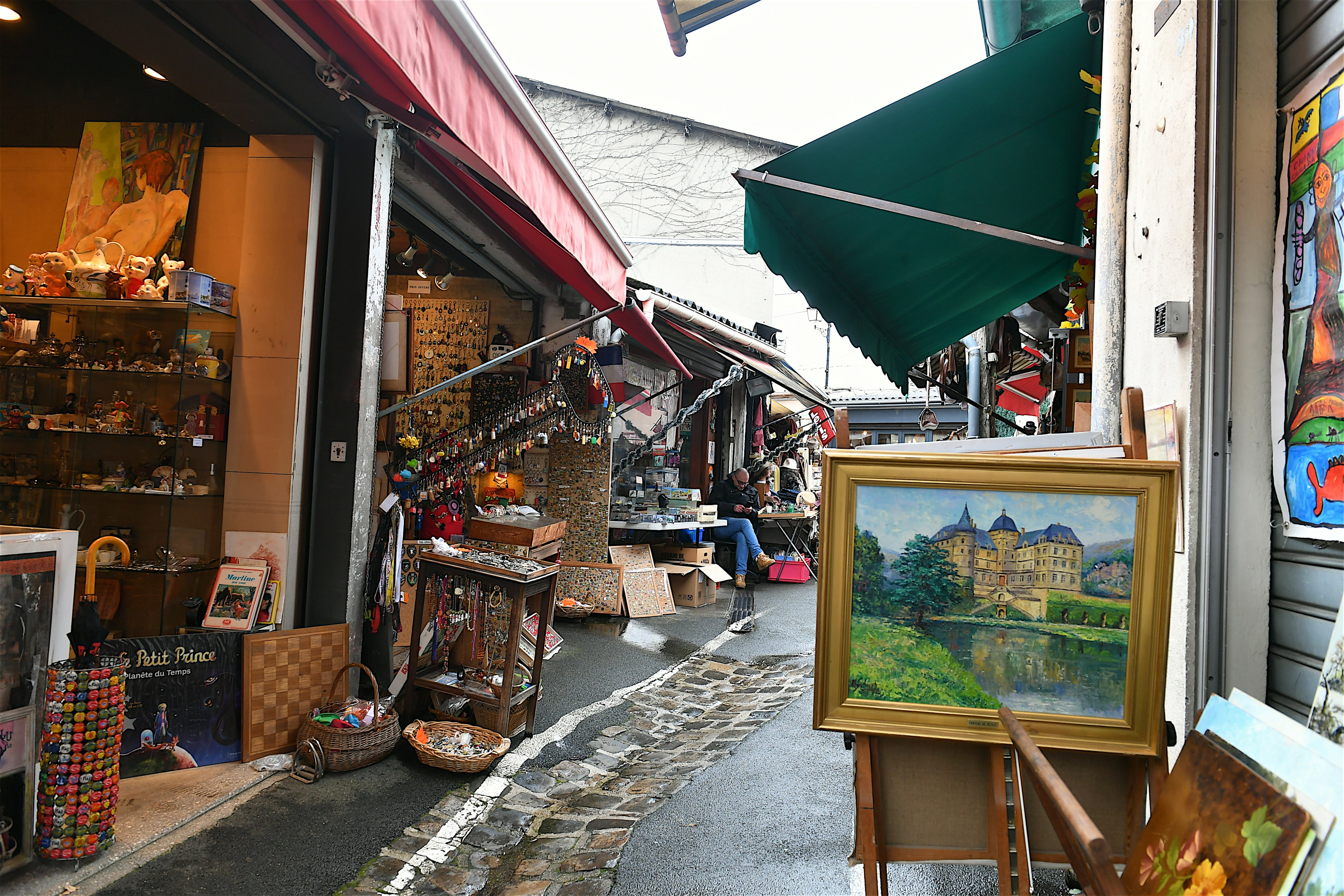 An alleyway in a market lined with stalls selling paintings, keyrings, posters, jewelry and bric-a-brac