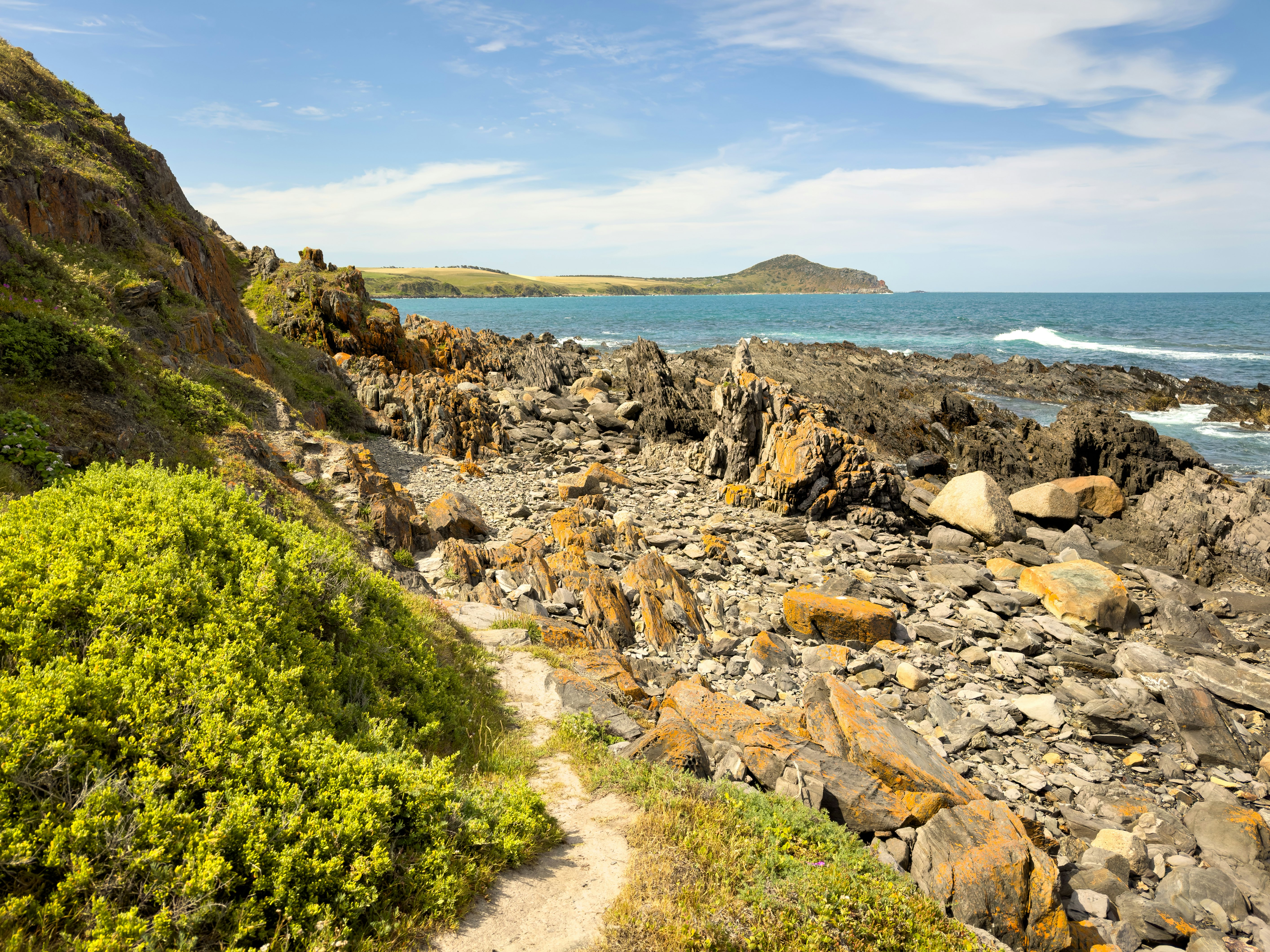 A sandy path winds its way between bush and rocks on a coastal hiking trail