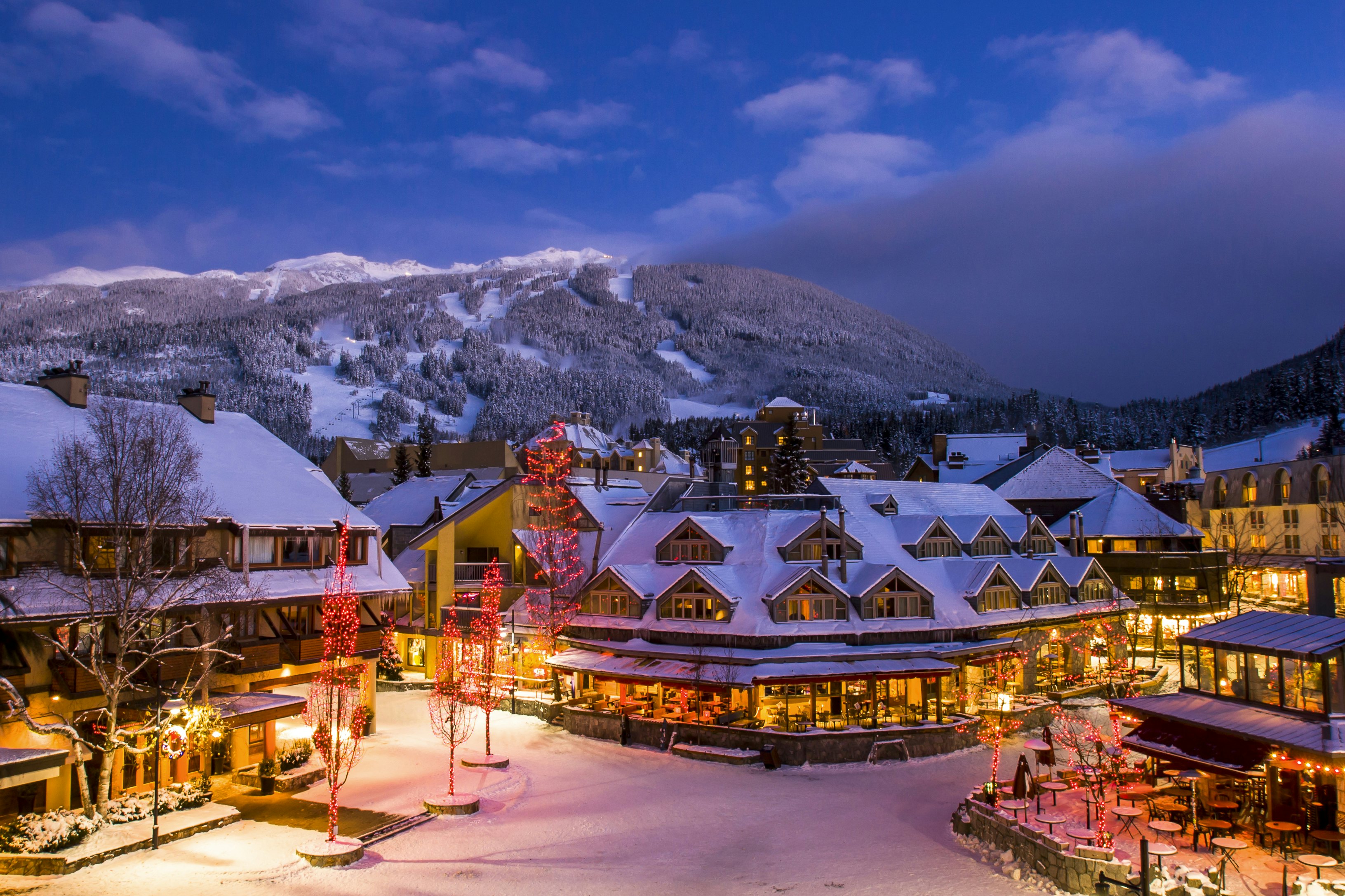 A snowy village in front of a large mountain at nighttime.
