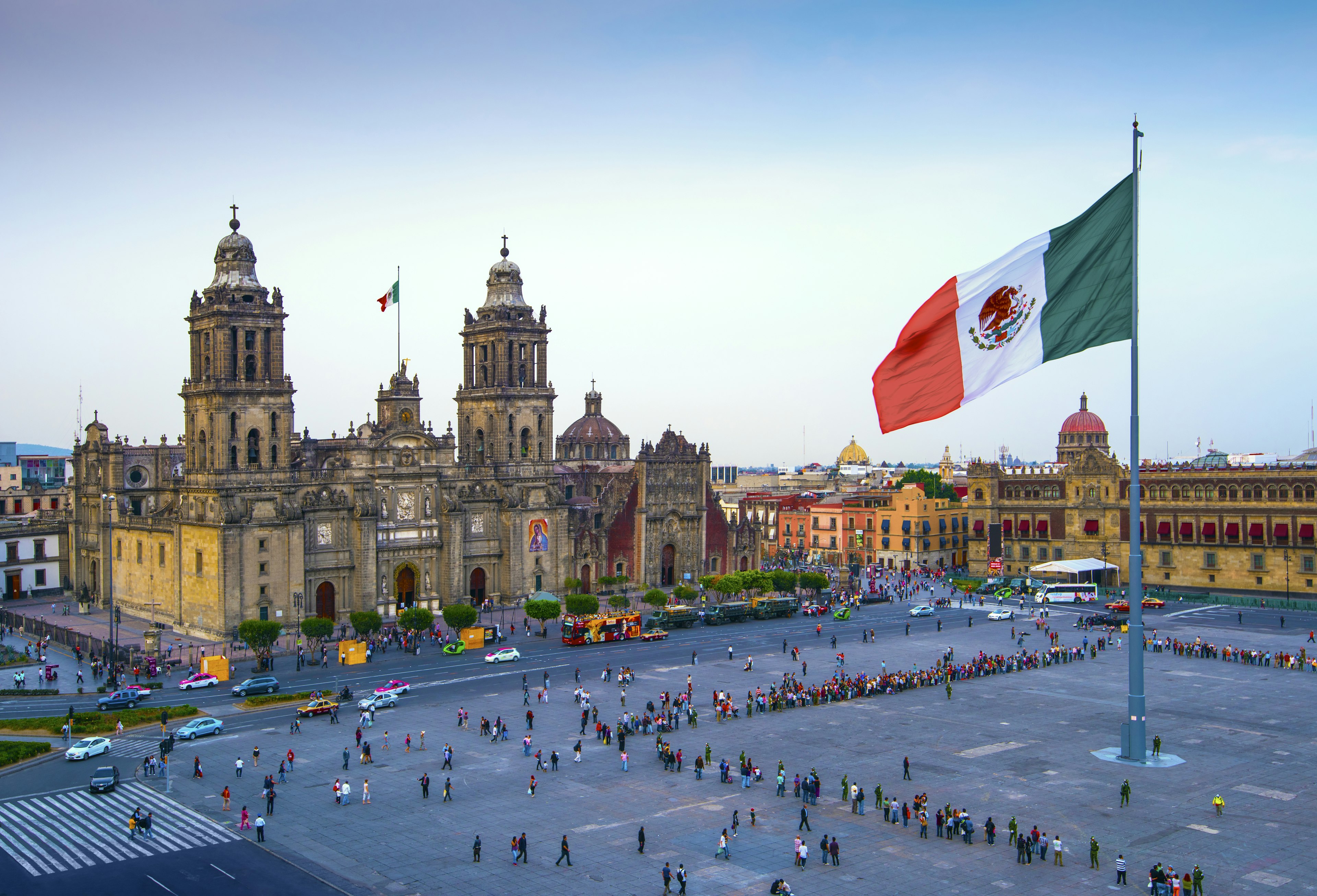 The Mexican flag flies over a large city square looked over by a cathedral