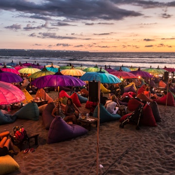 February 19, 2016: A crowd of people share food and drink under colourful umbrellas during sunset on Kuta beach.
628994390
Life, Landscape - Scenery, Editorial, Crowded, Nightlife, Crowd, Tree, Water, Southeast Asia, Lifestyles, Travel Destinations, Horizontal, Sky, Drink, Night, Dusk, Light - Natural Phenomenon, Photography, People, Building Exterior, Food, Asia, Tourist, Restaurant, Beach, Outdoors, Sea, Asian and Indian Ethnicities, Kuta, Parasol, Bar - Drink Establishment, Walking, Nature, Tourist Resort, Indonesia, Seminyak, Beer Bottle, Sofa, Majestic, Famous Place, Sand, East Asian Ethnicity, Tourism, Bali, Young Adult, Landscape, Mass - Unit of Measurement, Fun, Party - Social Event, Travel, Beach Party, Sunset, East Asian Culture, Arts Culture and Entertainment, Backpacker