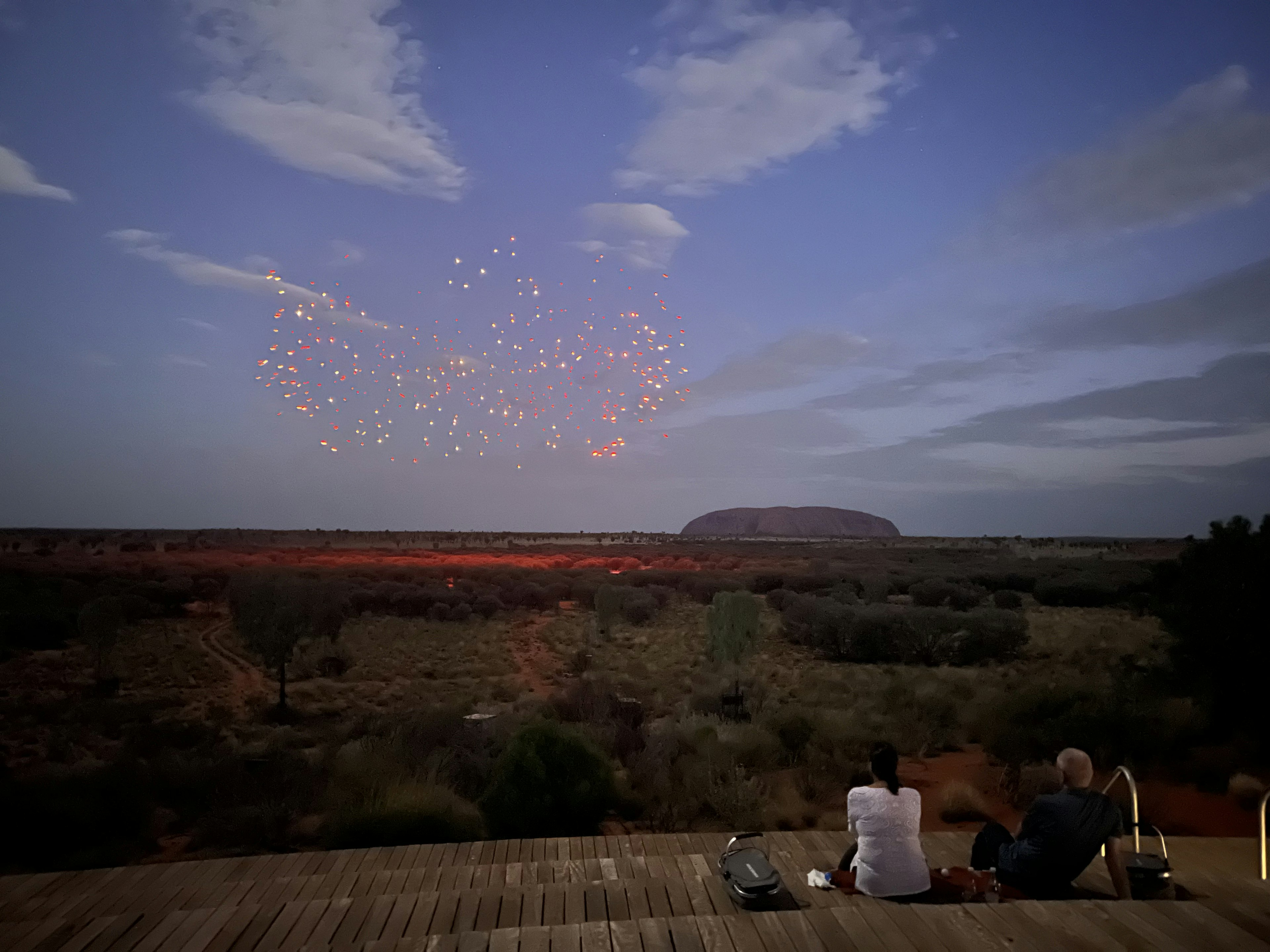 Drone in the sky form part of a light show with the ancient rock of Uluru in the distance.