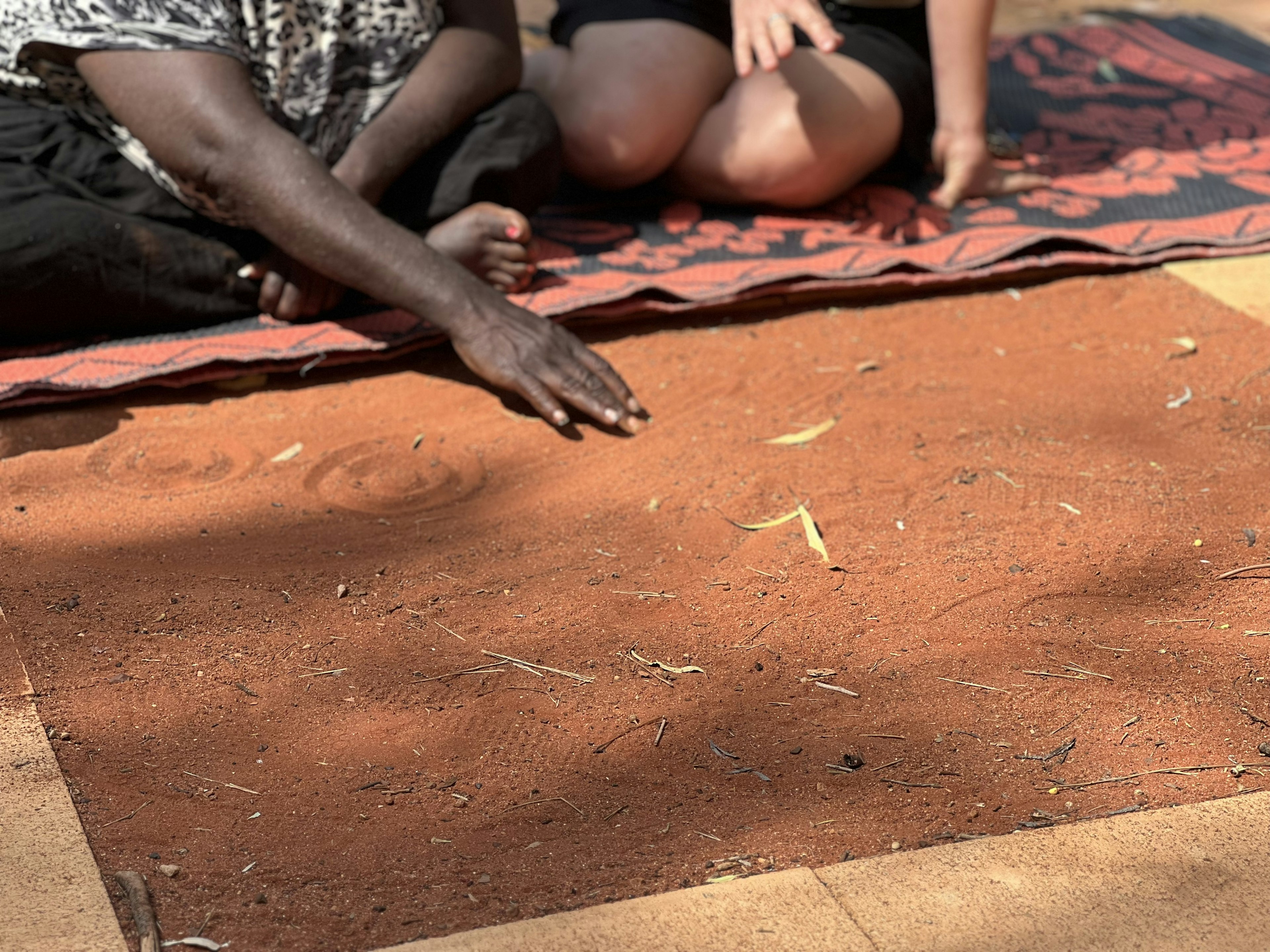 An Anangu artist demonstrates symbology by drawing with their hands in red sand