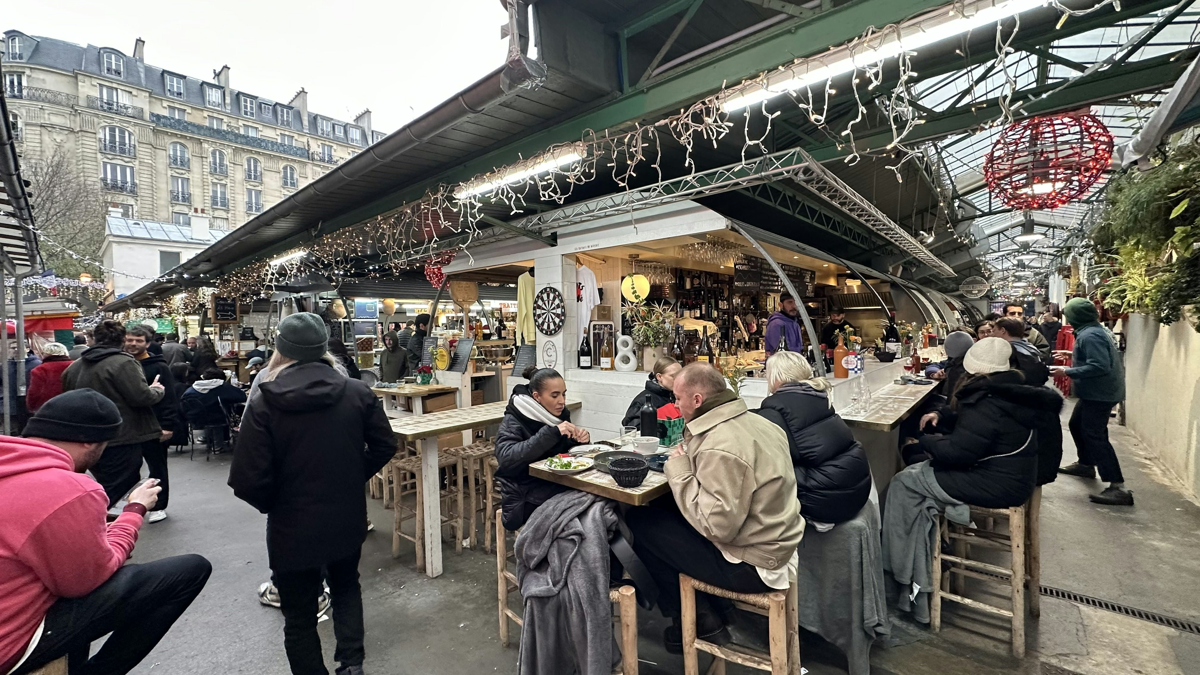 Diners sit at tables near stalls in a covered food market