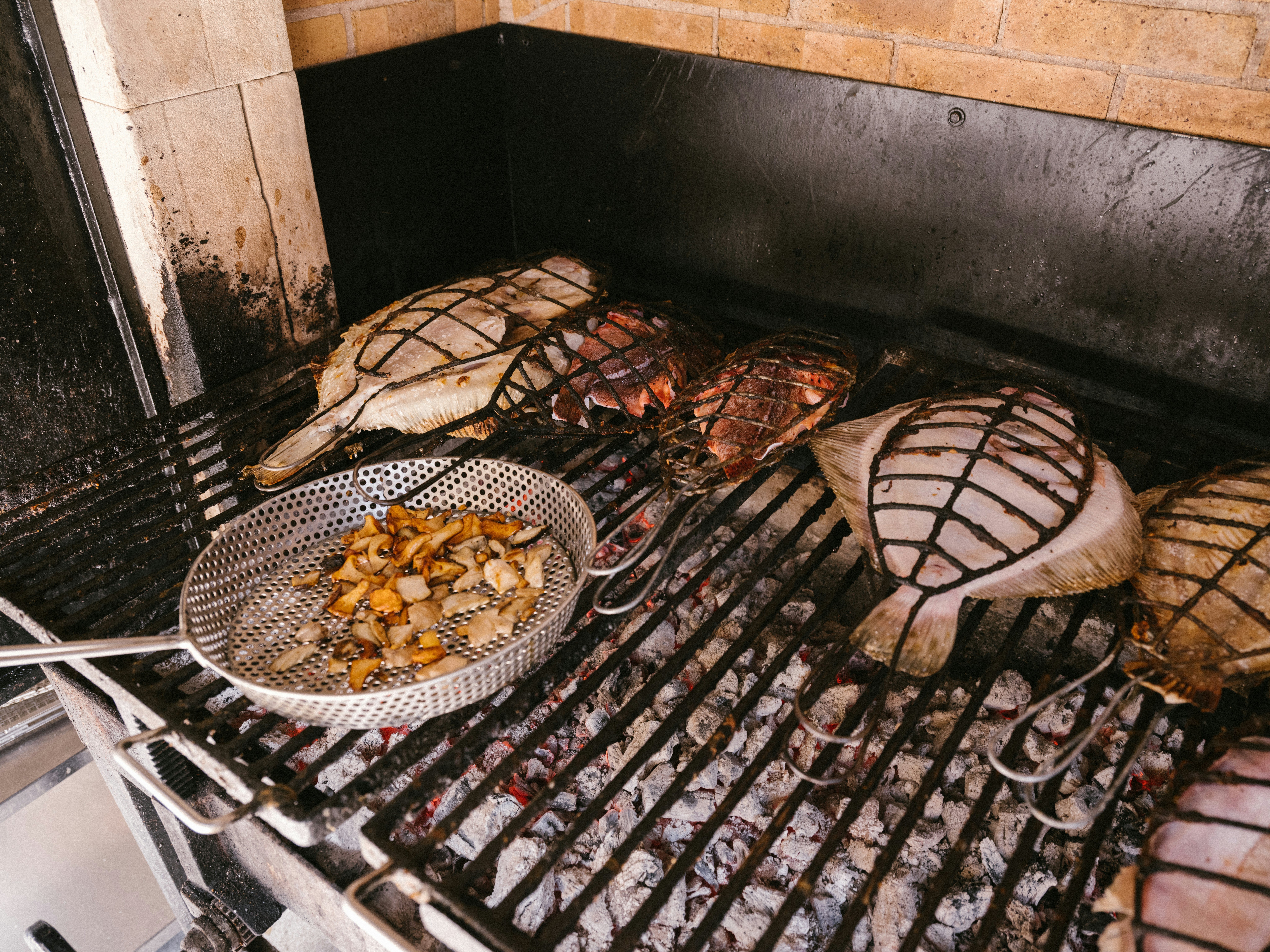 Fish and a pan with vegetables cool on a charcoal grill in the kitchen of a restaurant.