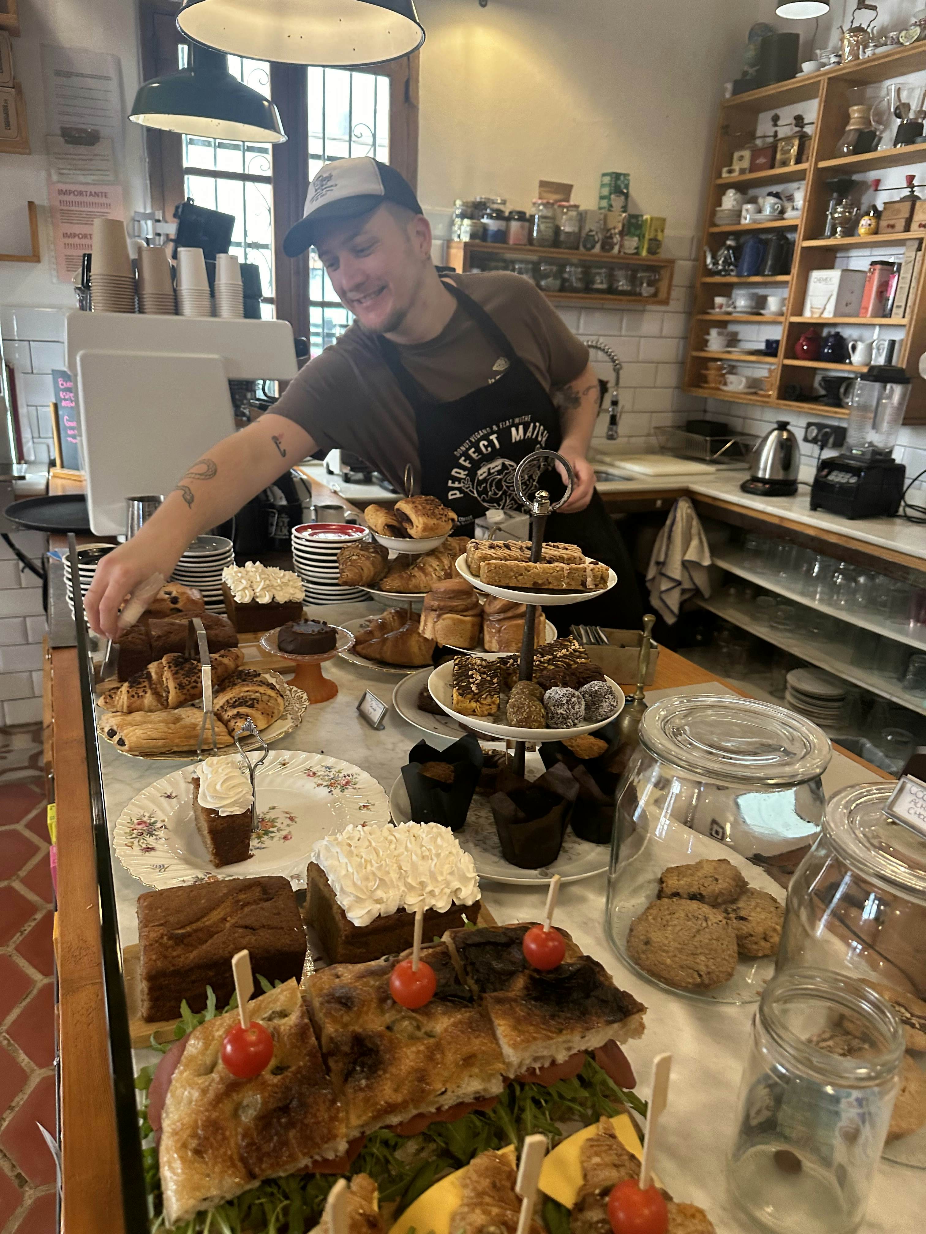 A server wearing a black T-shirt and full blue apron. She is carrying two plates of food on her arm