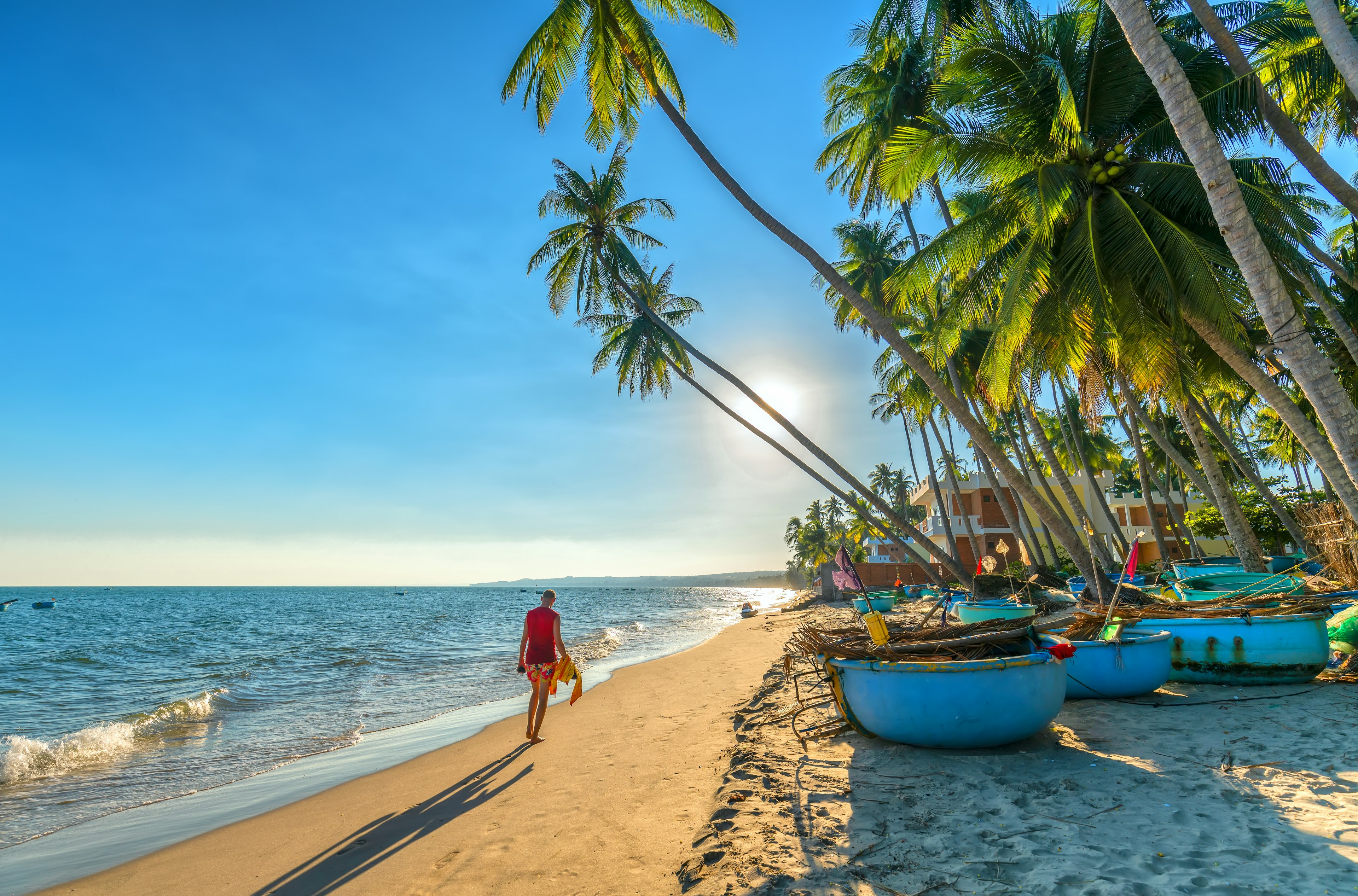 A tourist walking underneath palm trees on the beach at Mui Ne, Vietnam.