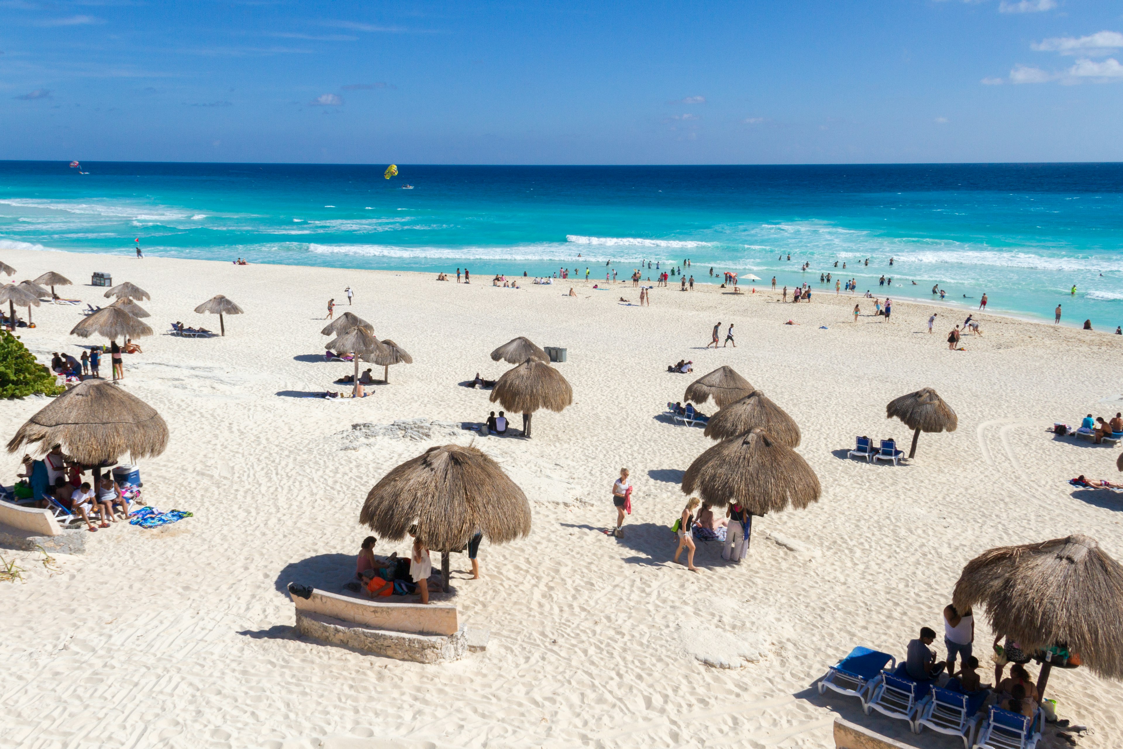 People under thatched umbrellas on the sand at Playa Delfines, Cancun, Mexico.