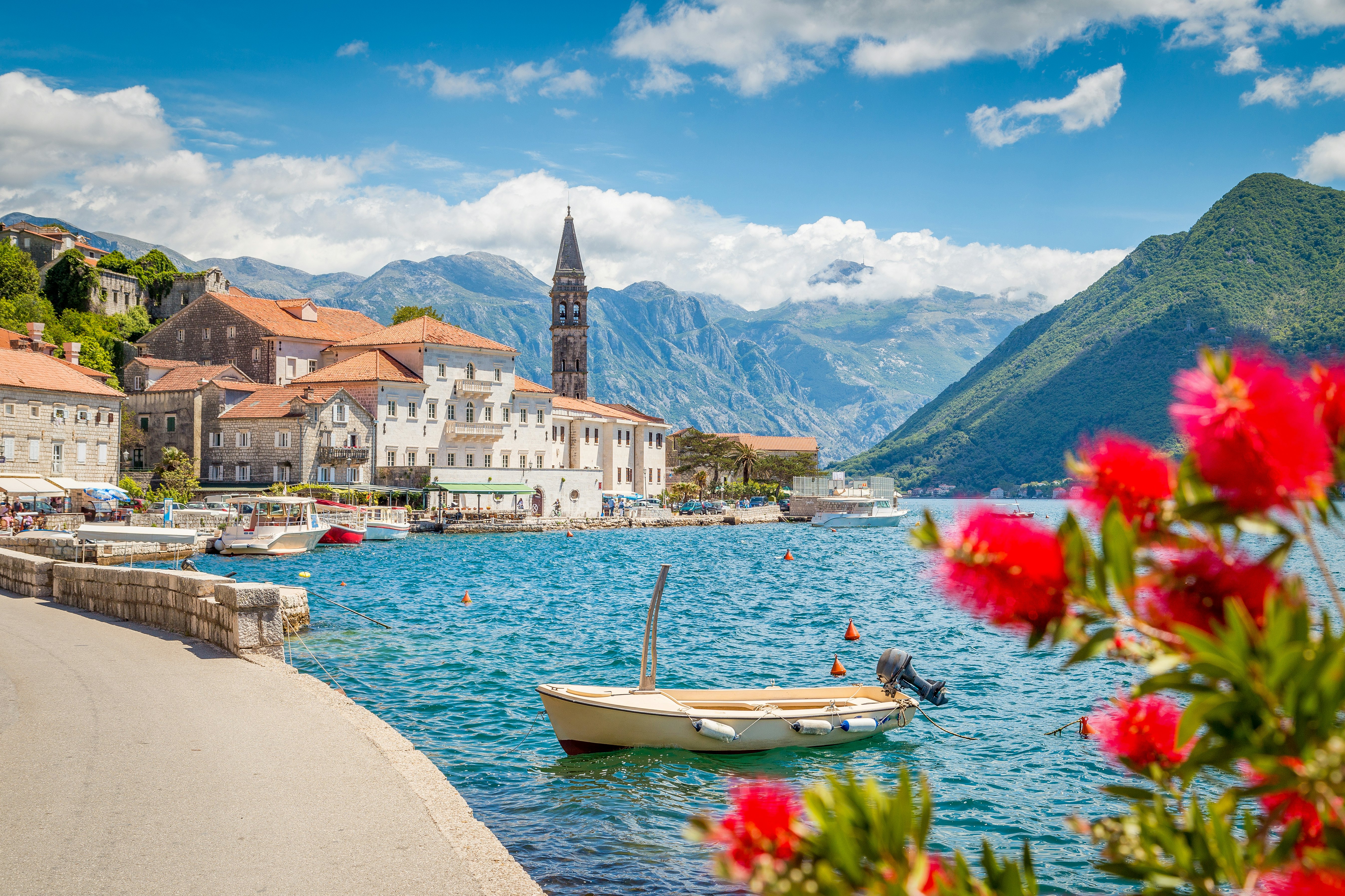 A scenic panorama view of the historic town of Perast at the famous Bay of Kotor with blooming flowers on a beautiful sunny day with blue sky and clouds in summer, Montenegro