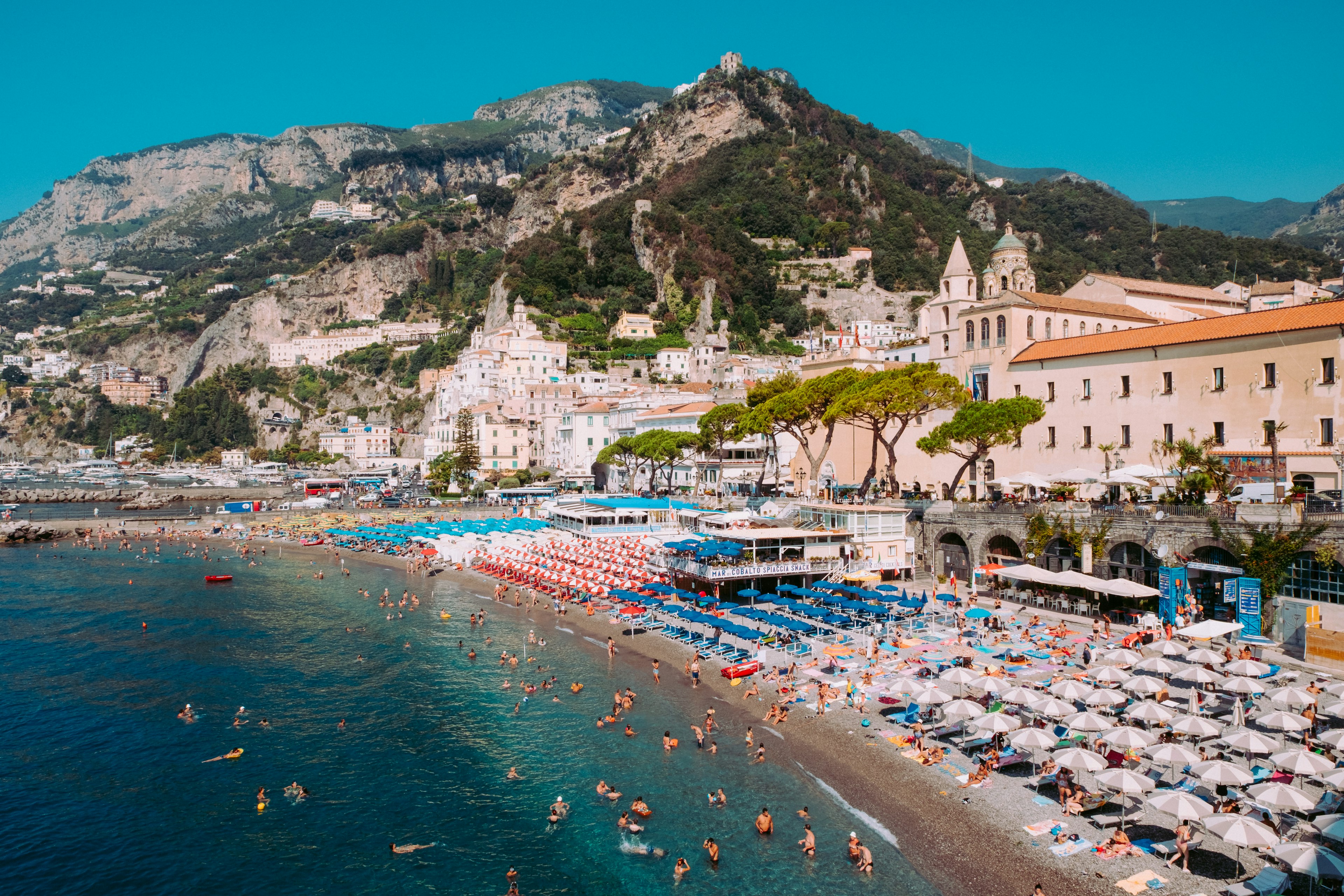 A scenic view on Amalfi town beach with mountains in the background and people swimming in the sea.