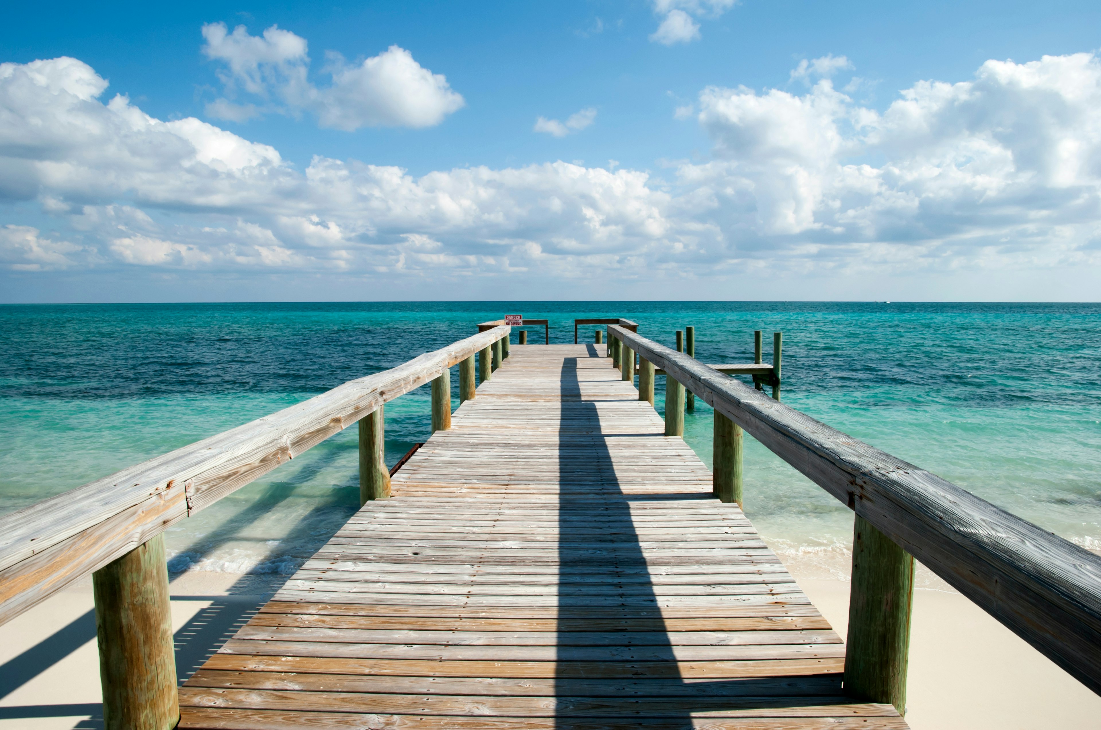 The view of Caribbean Sea and the wooden pier with a warning sign on Taino Beach, Grand Bahama Island.