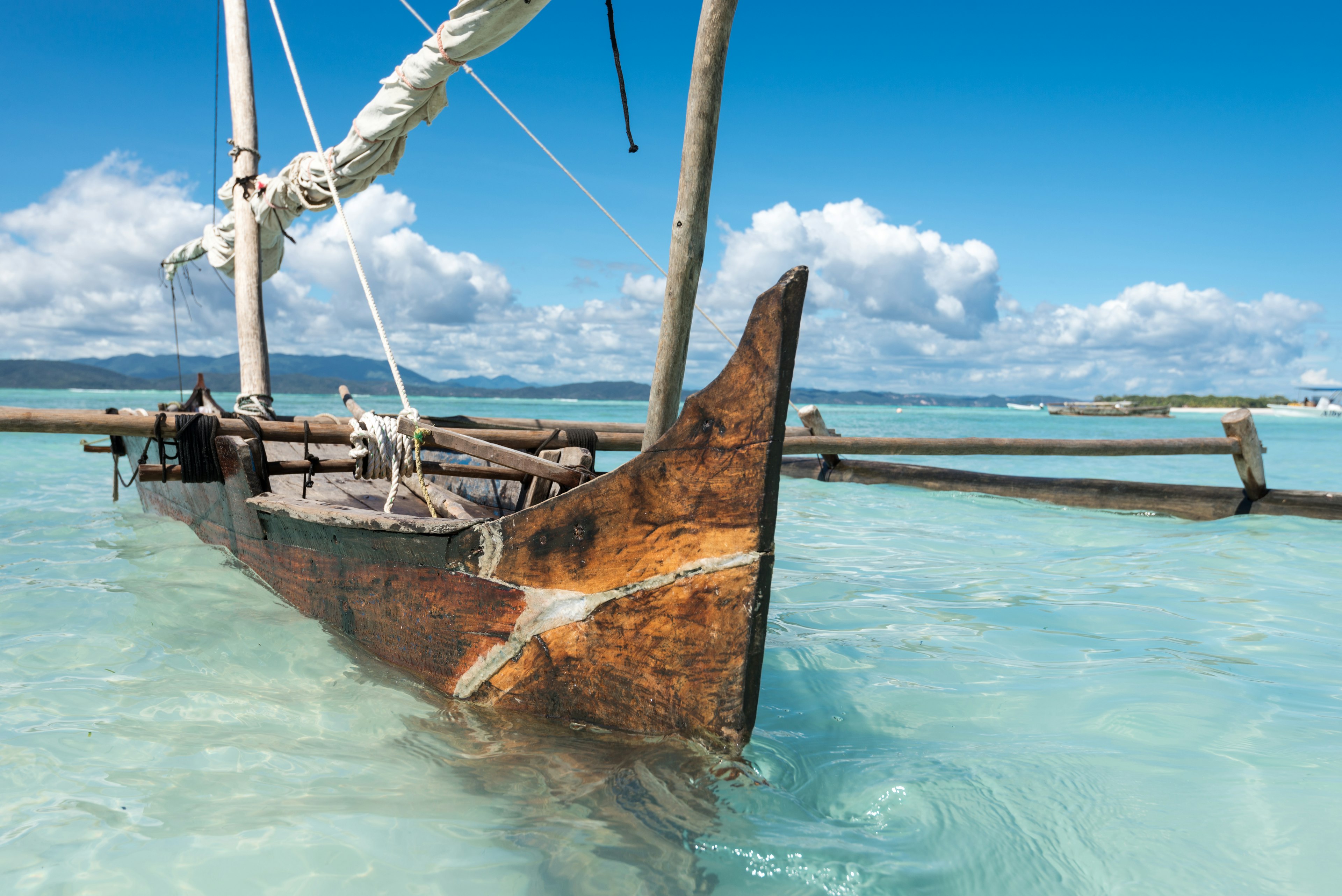 A WOODEN SAILBOAT WITH PONTOONS IS MOURED in Crystal-Clear Water Near a Tropical Beach.