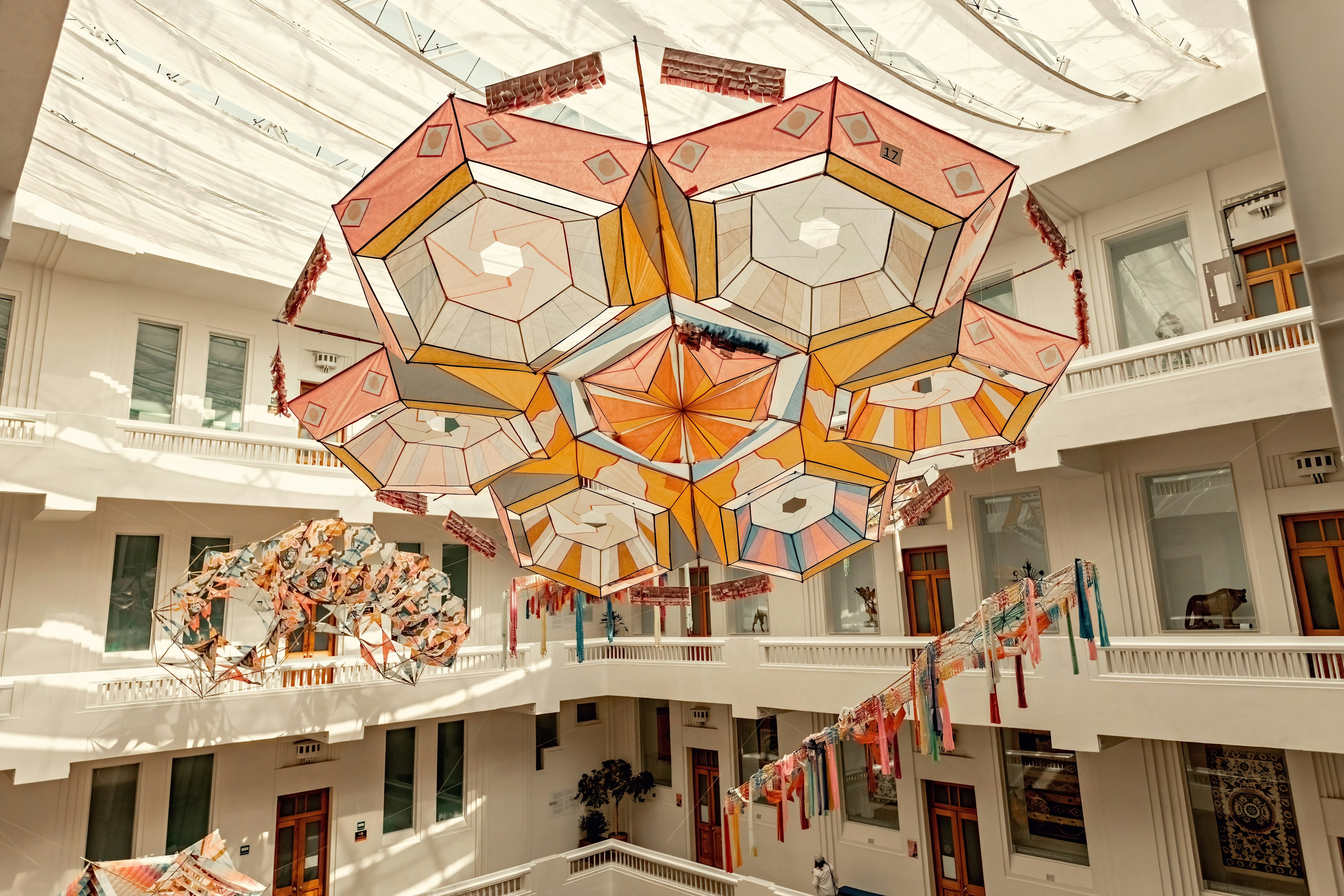 A large sculpture made of fabric in geometric shapes hangs from a ceiling in a central atrium of a museum