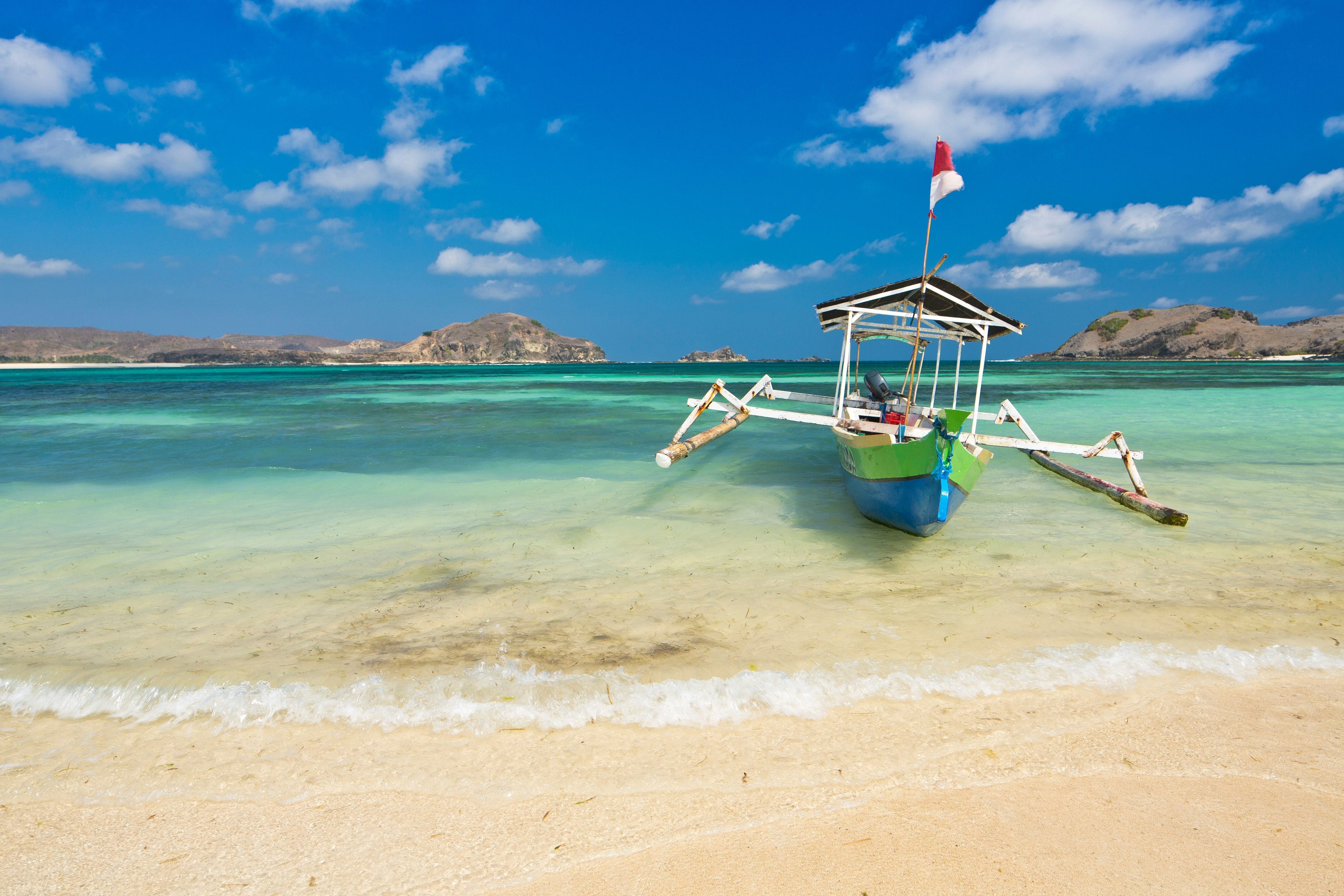 An outrigger boat on a beach in Indonesia with a view of islands beyond.