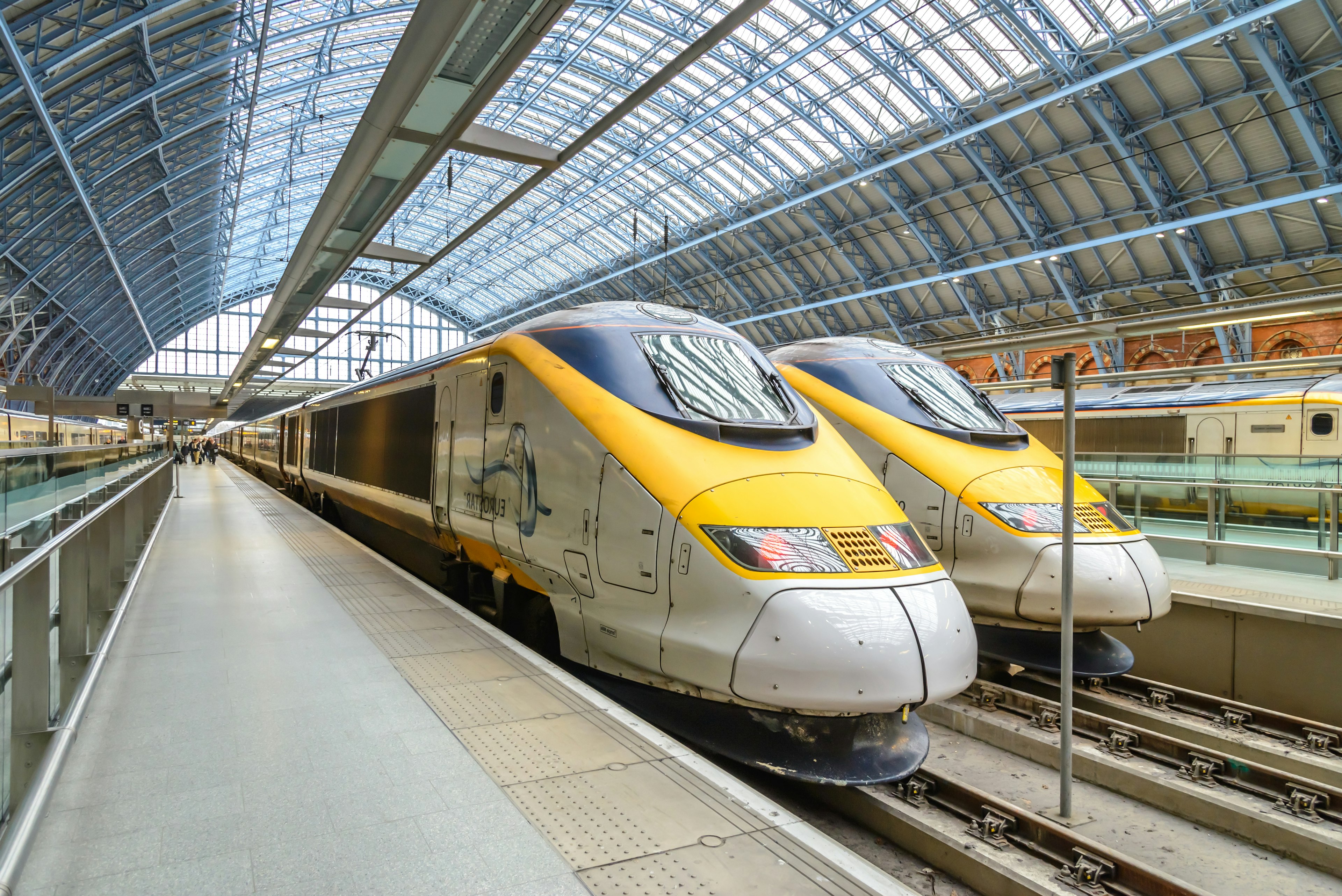 Two trains stand at platforms in a station with a glass roof