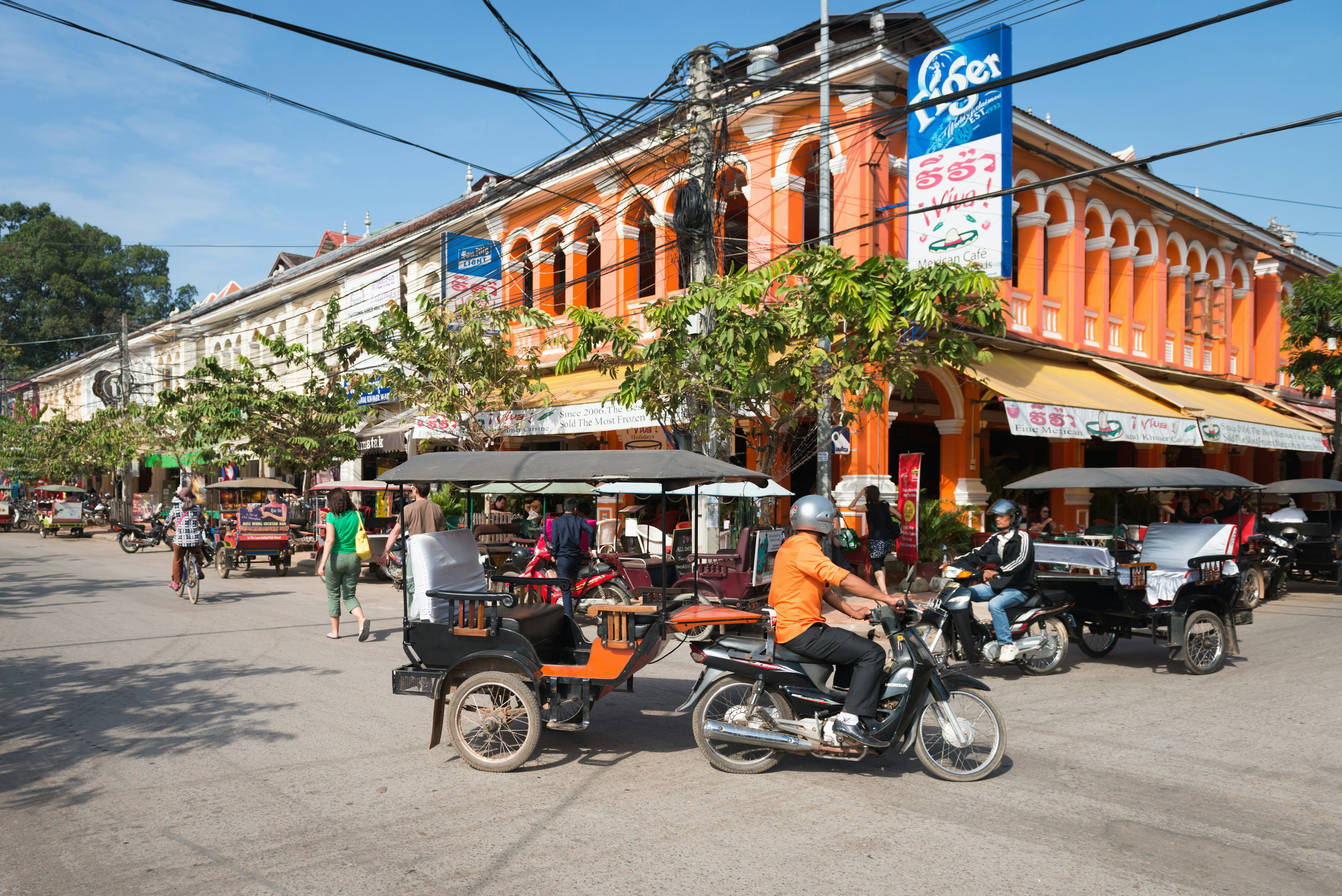 SIEM REAP, CAMBODIA - 23 DEC 2013: Tuk-tuk tourist taxi on the central street of the town with colonial architecture buildings  License Type: media  Download Time: 2023-08-01T14:10:00.000Z  User: FergalCo  Is Editorial: Yes  purchase_order: