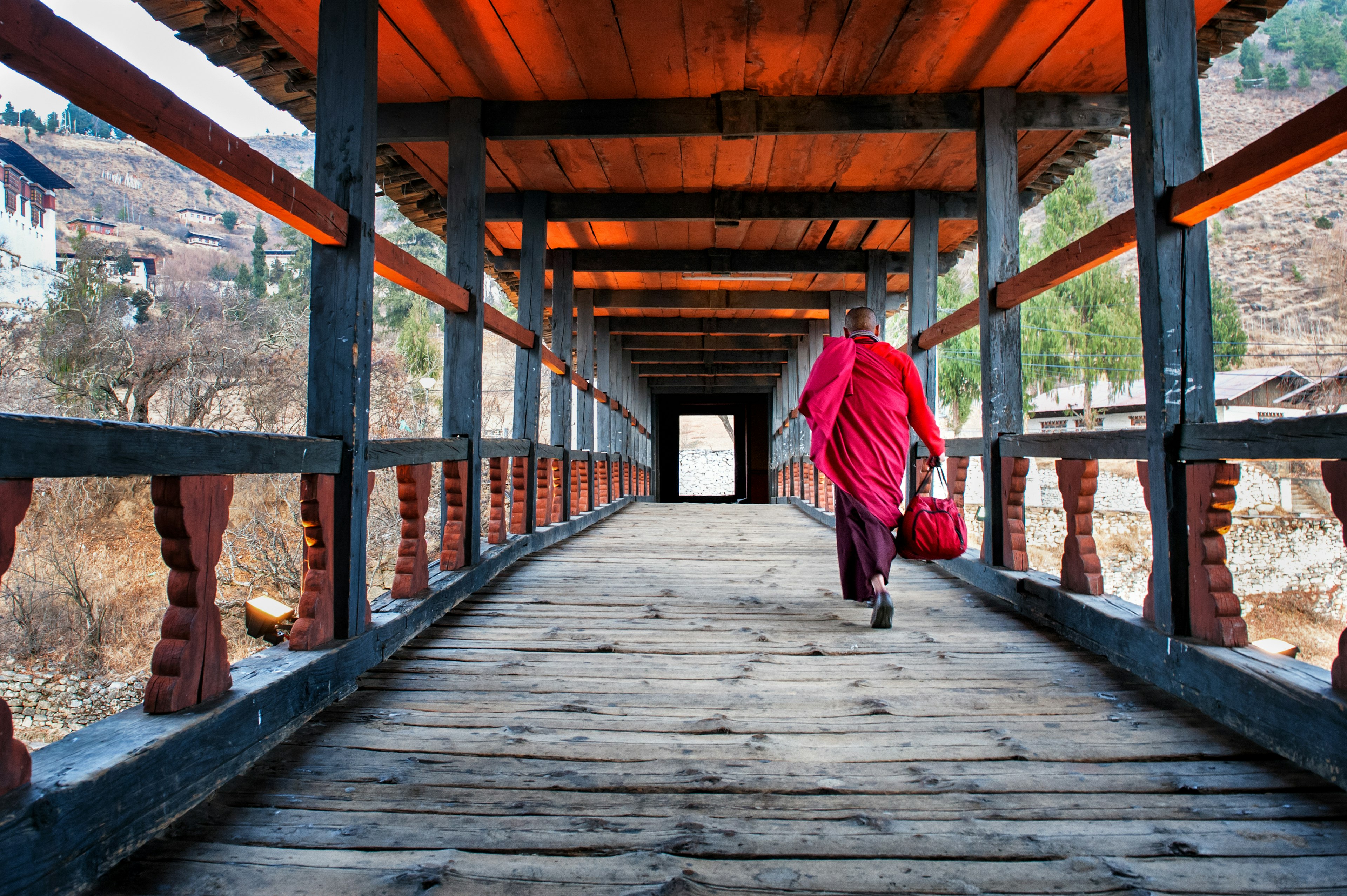 A monk in a pink robe crosses a covered wooden bridge