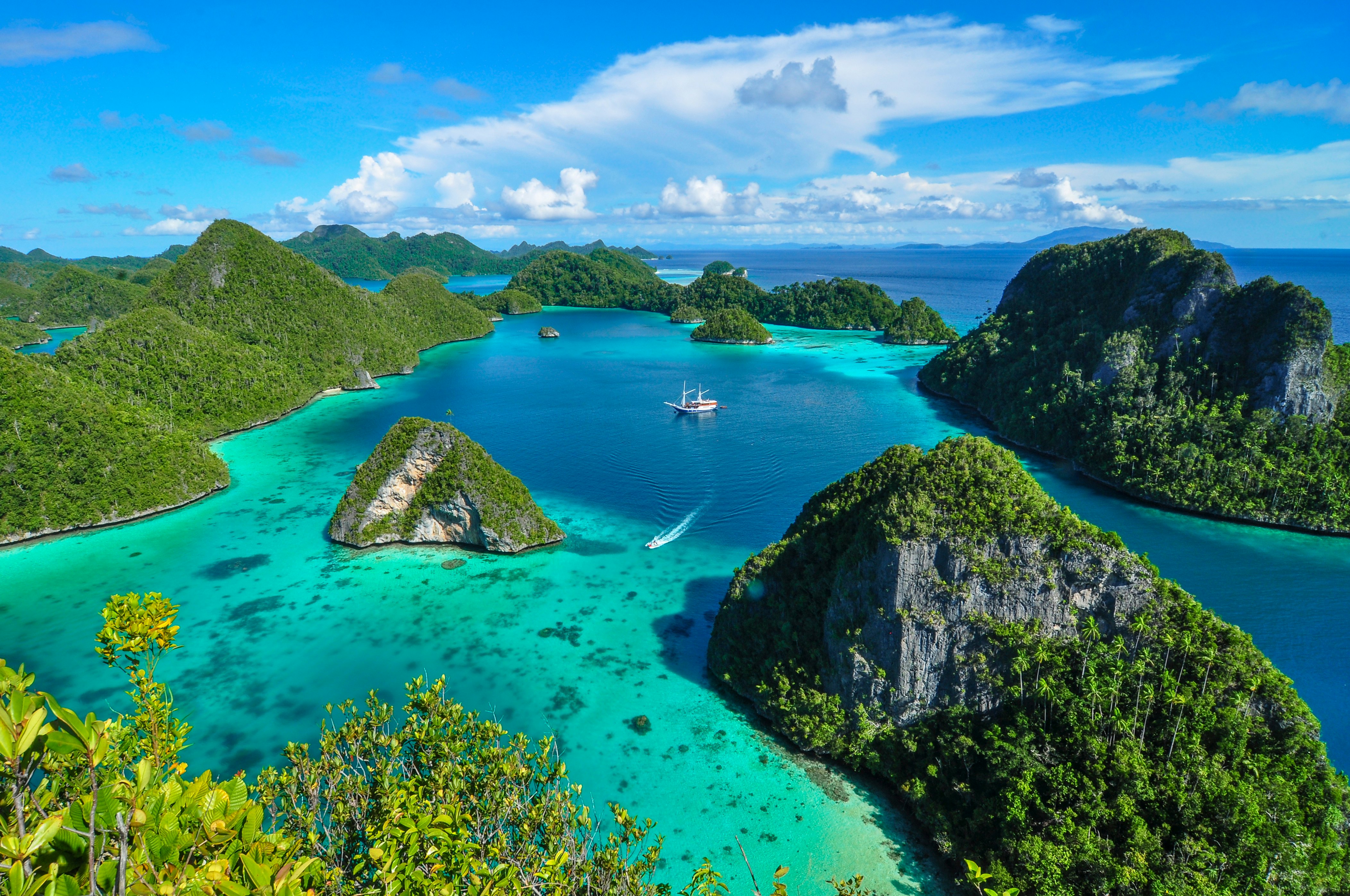 A few boats sail within a lagoon of turquoise and blue water at Wayag in Raja Ampat, Indonesia