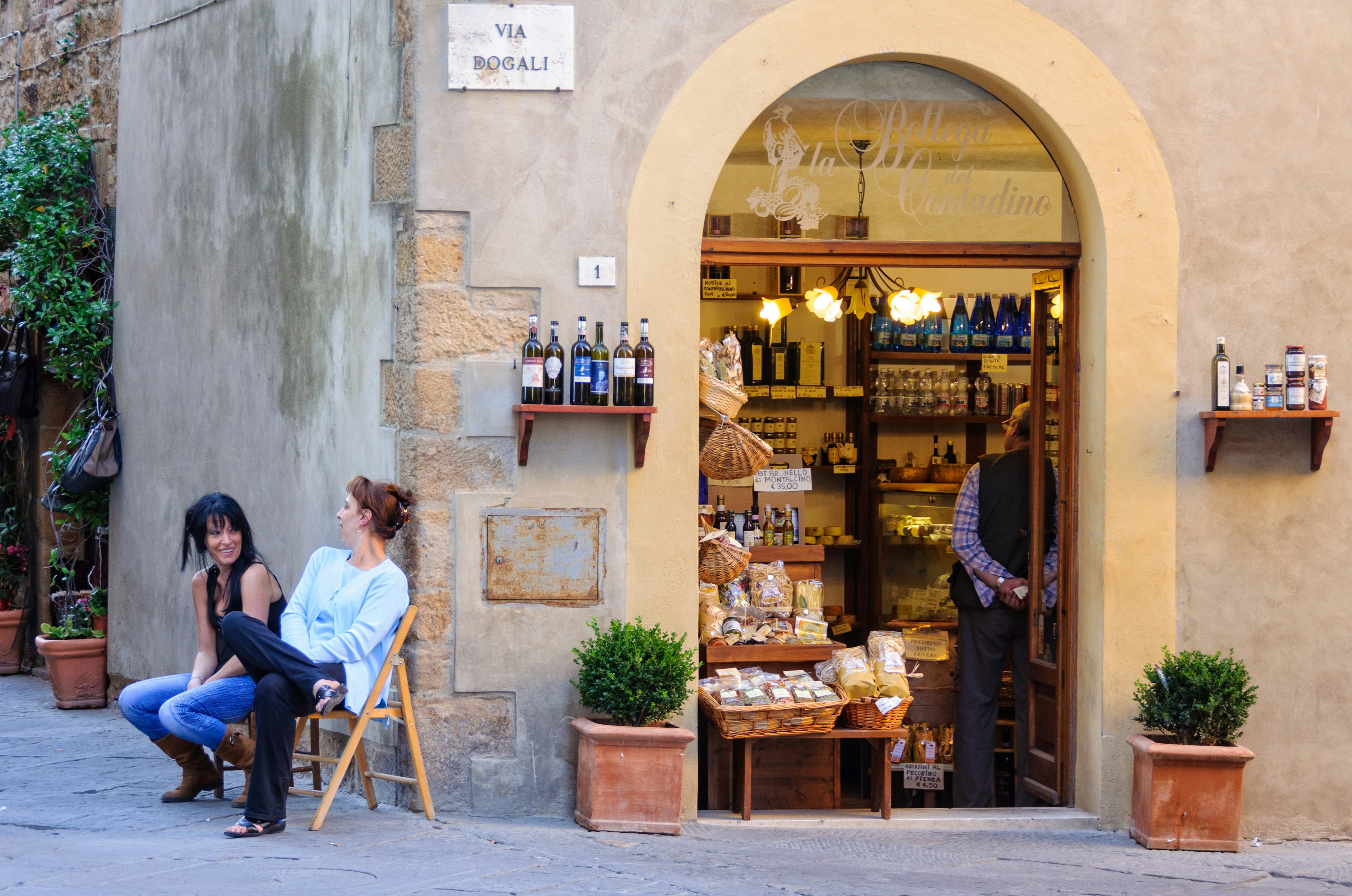 Two women having a chat on chairs outside a gourmet food shop.