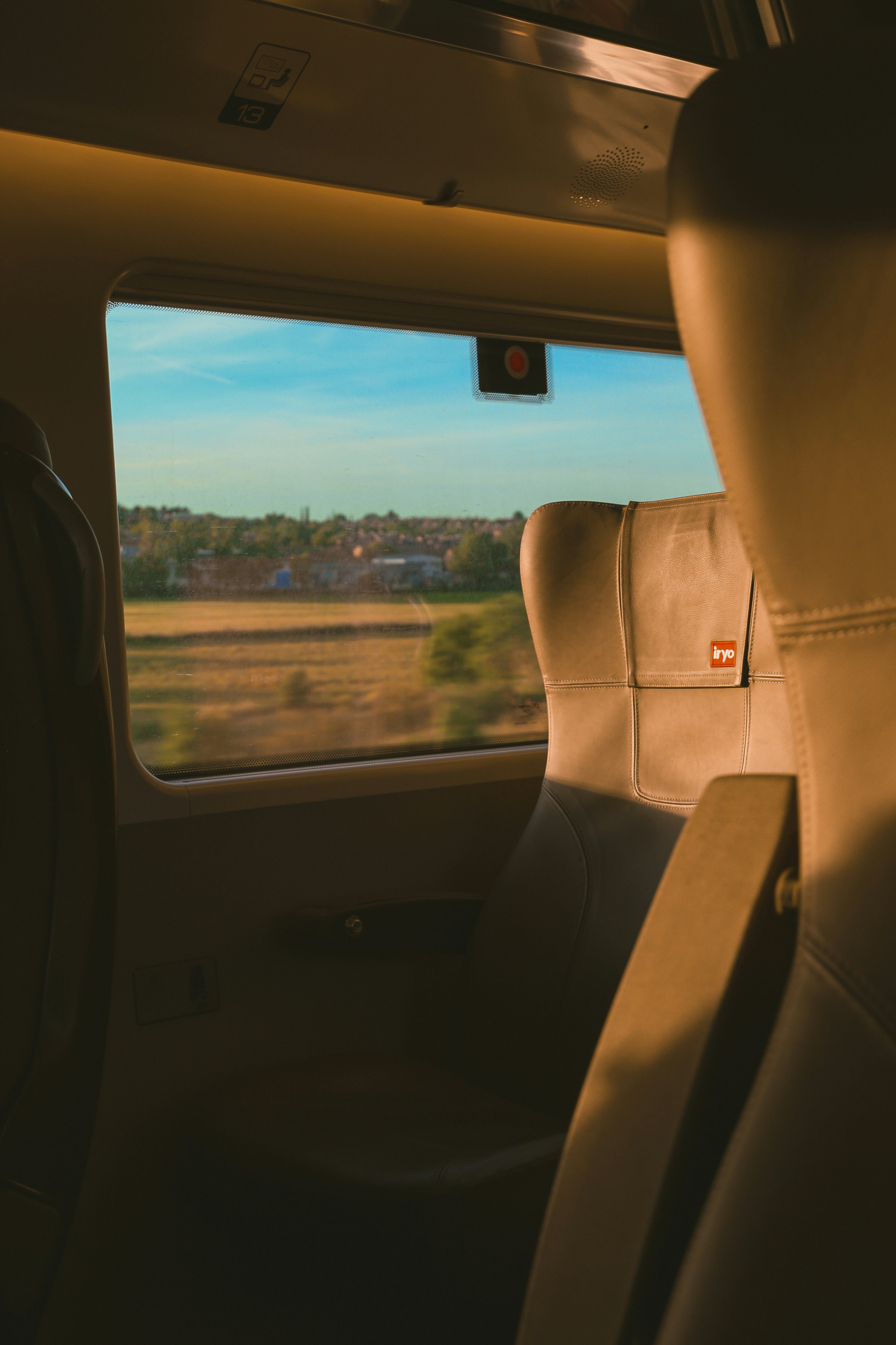An empty window seat on a train passing fields bathed in sunlight at high speed.
