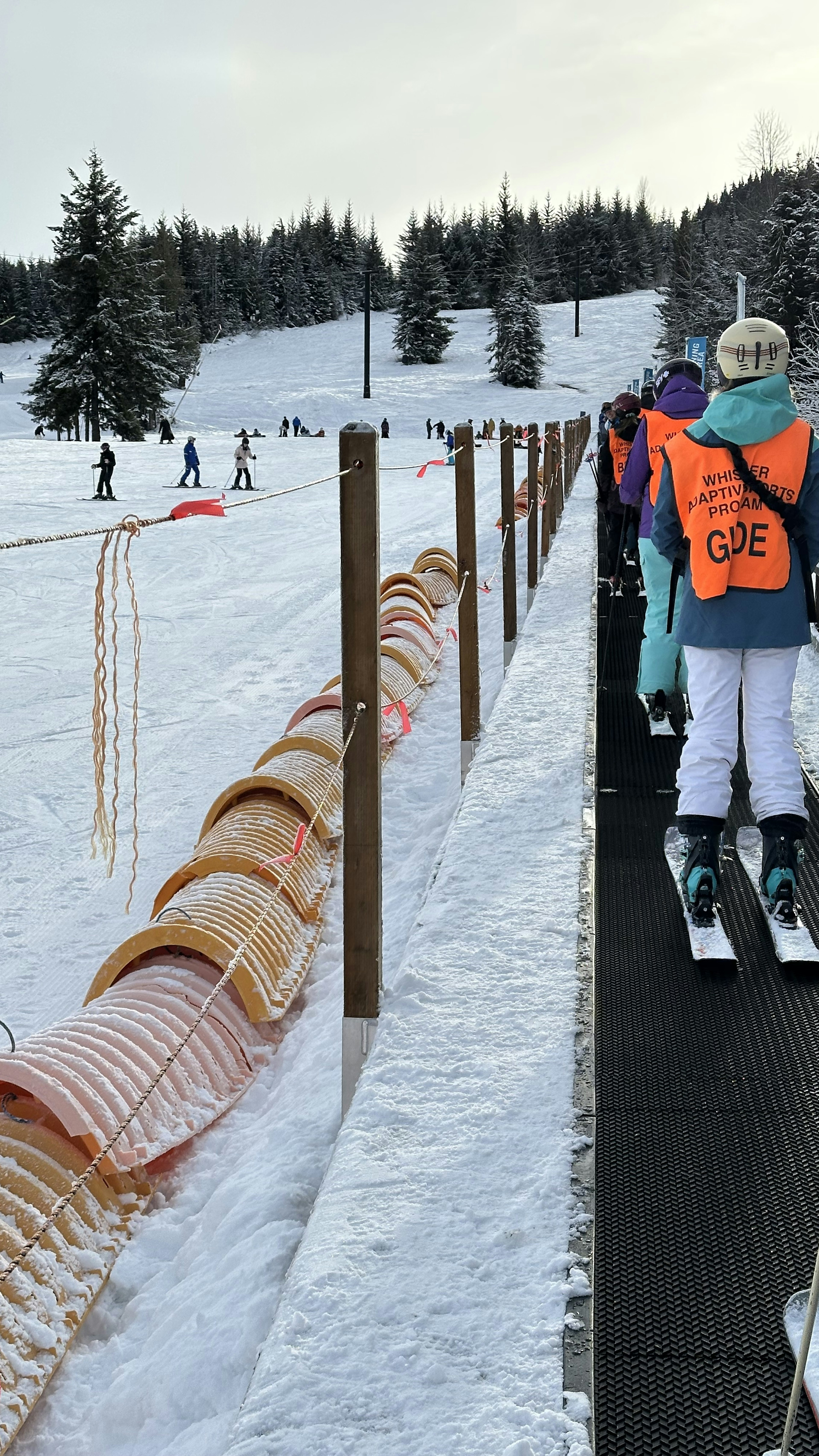 Adaptive guides in orange vests lead a ski lesson on a snow-covered slope