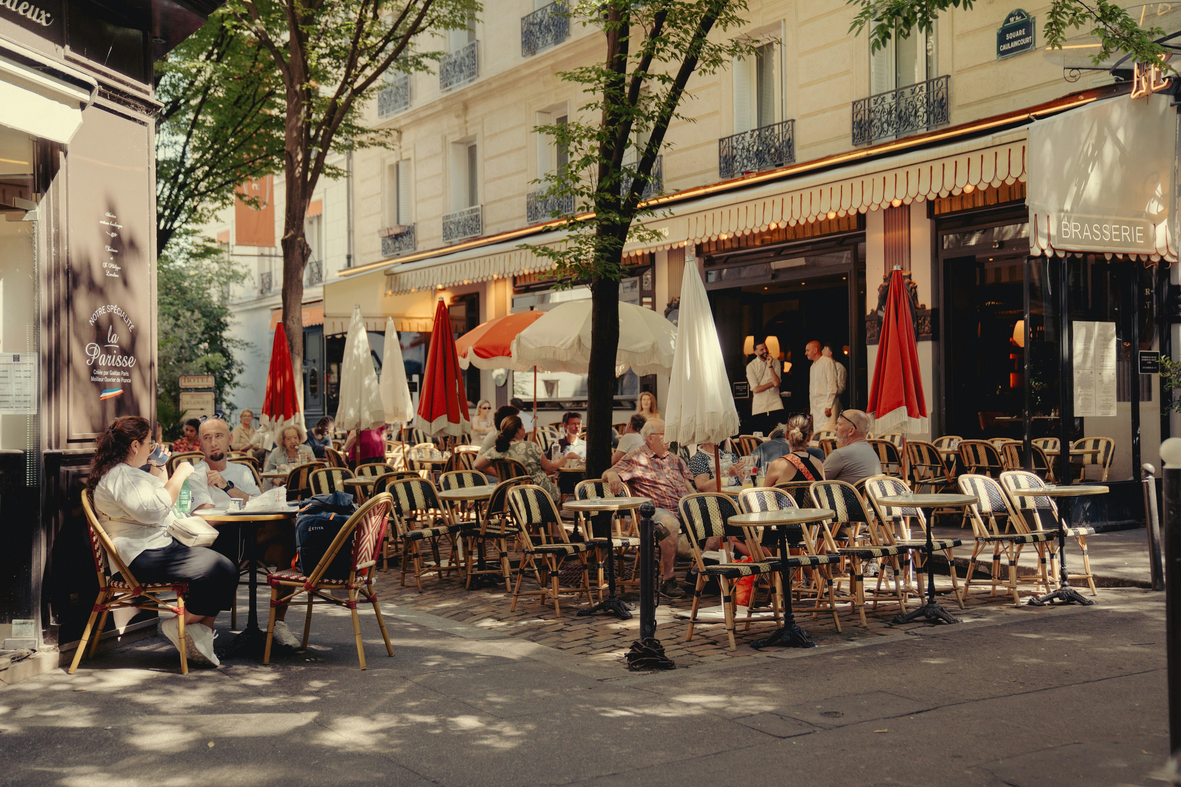 People sit on chairs on a terrace in the sun outside a bistro